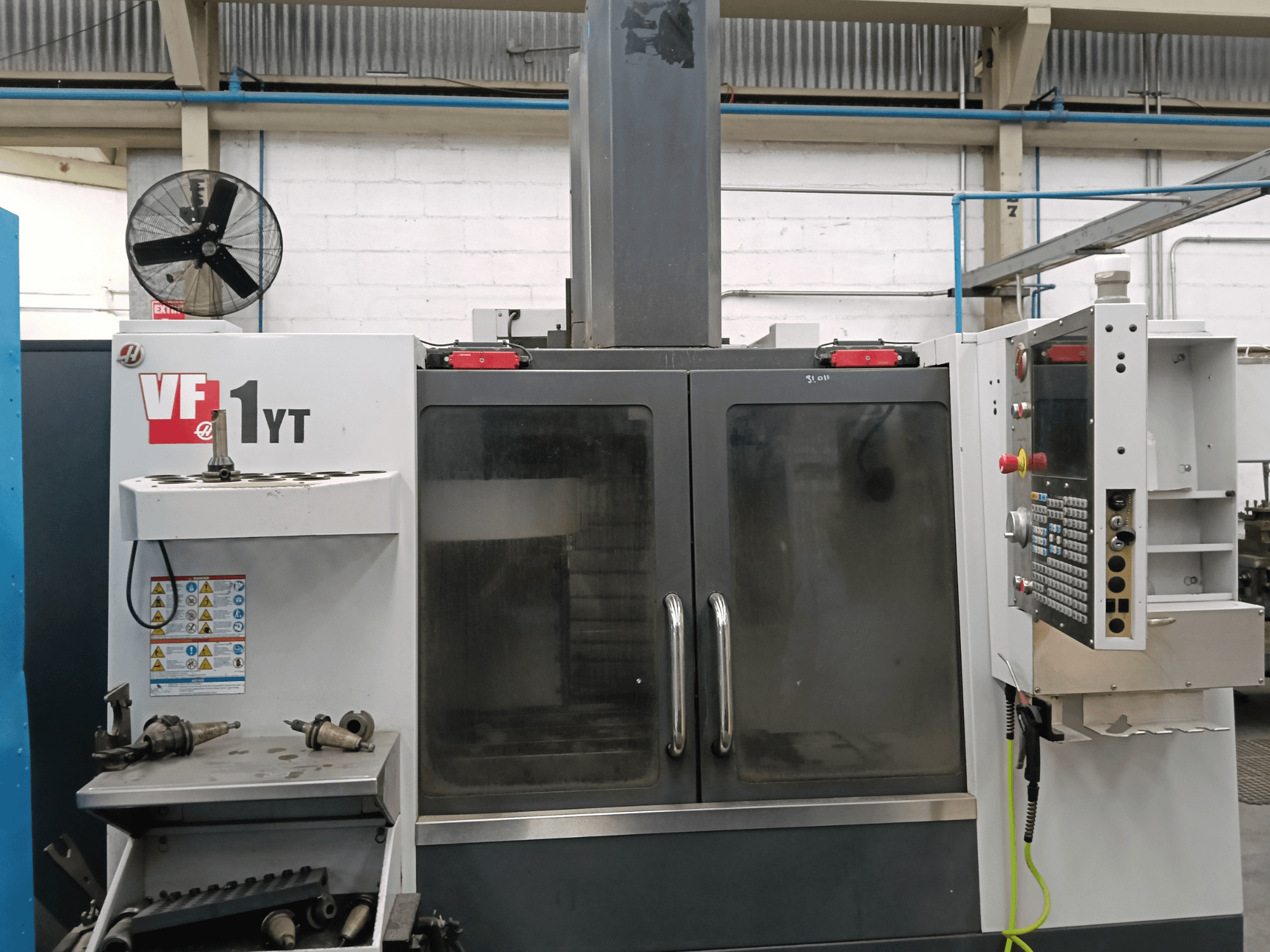Vooraanzicht van het verticale bewerkingscentrum HAAS VF-1YT-1 met bedieningspaneel en gereedschappen aan de zijkant.