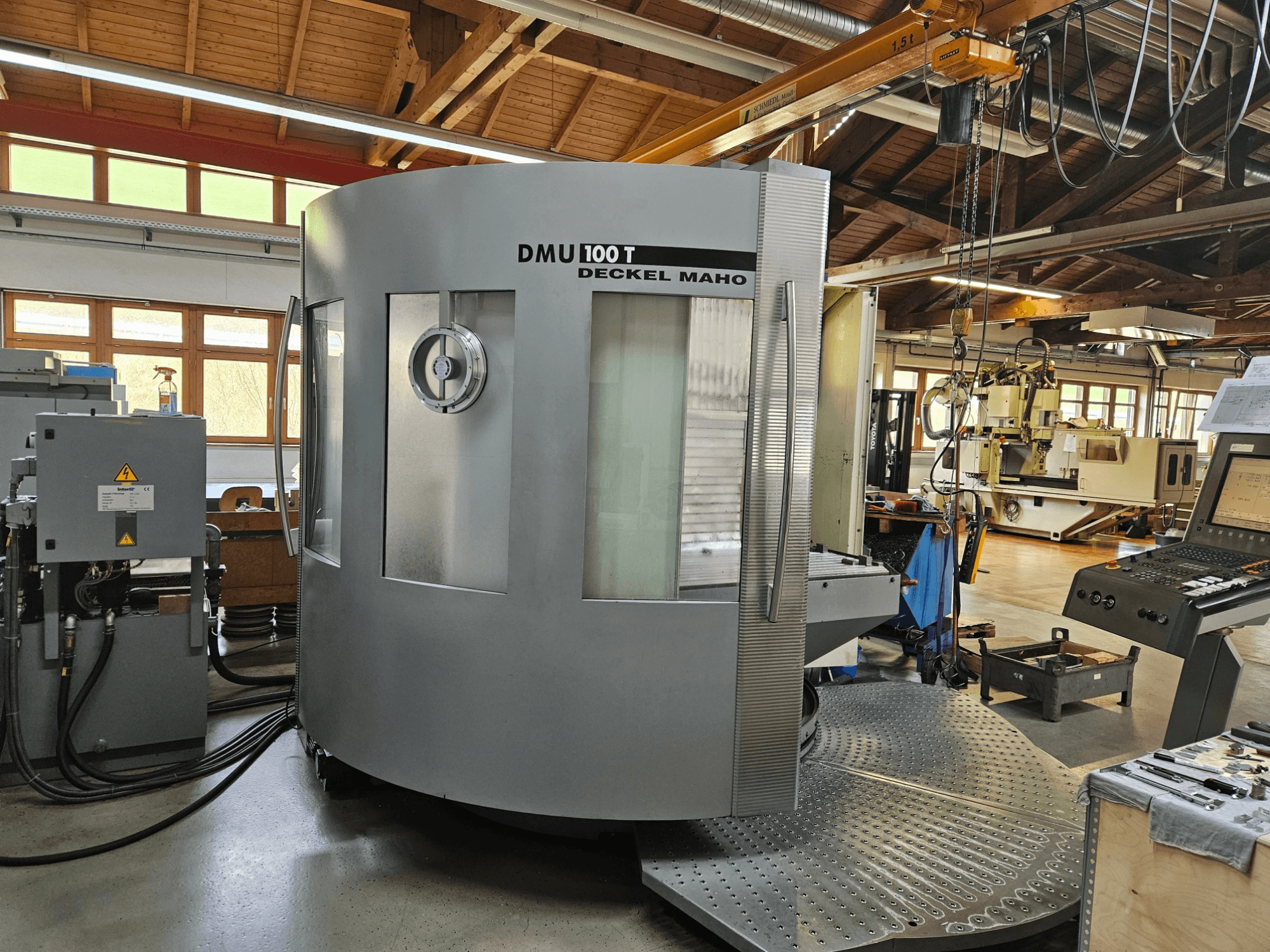 DMU 100 T Deckel Maho CNC machine gezien vanaf de voorkant, met een grote ronde voet, bedieningspaneel en glazen behuizing.