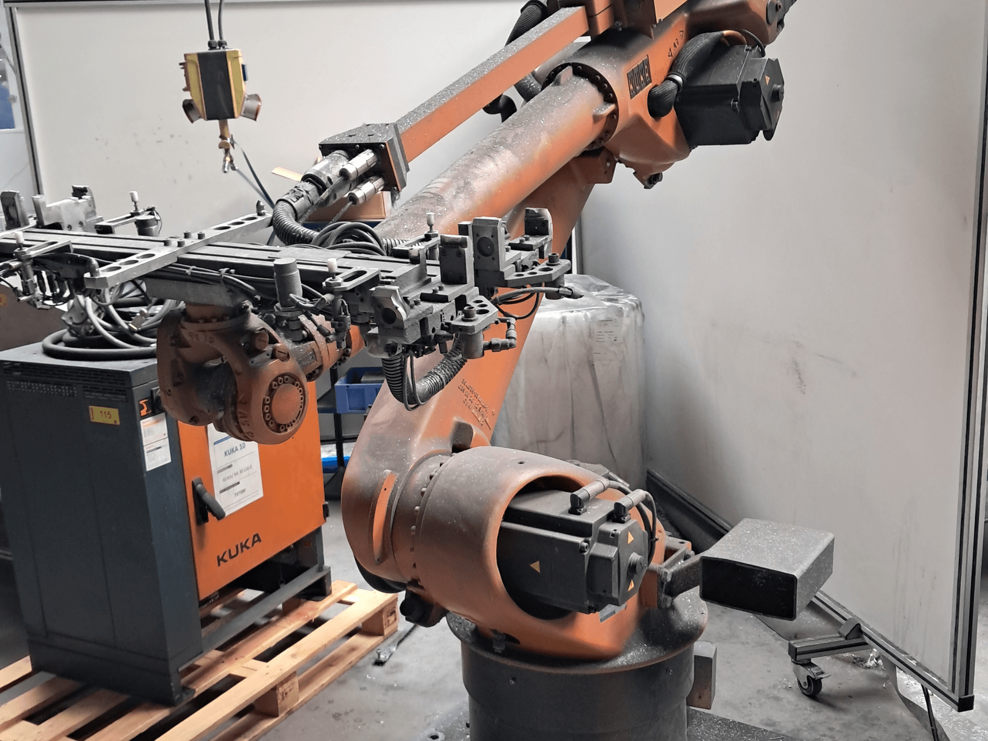 KUKA KR 30L16-2-robotarm in zijaanzicht, met een complex eindgereedschap en besturingskabels, naast een KUKA-besturingskast.