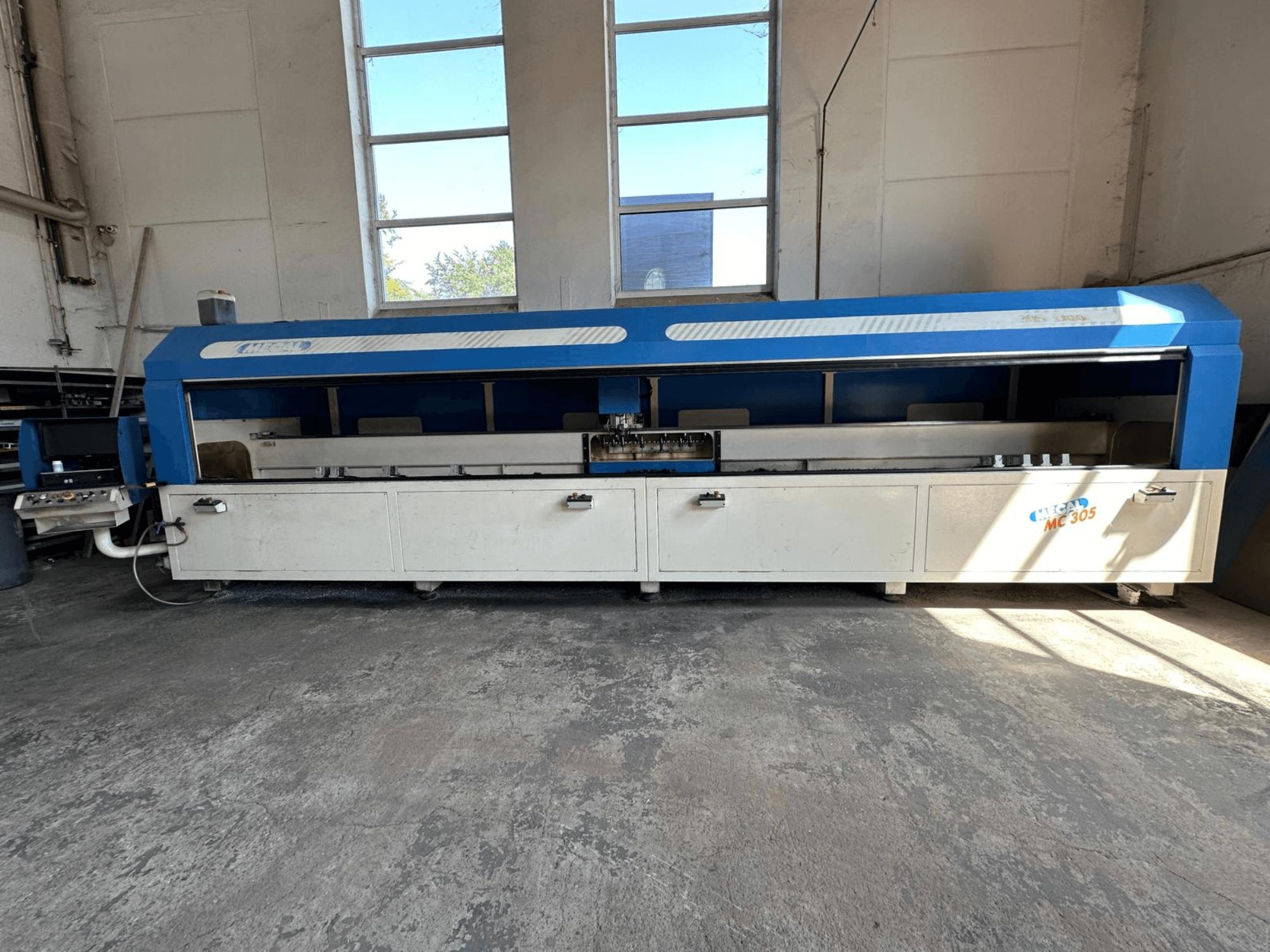 Vooraanzicht van MECAL MC 305 verticaal bewerkingscentrum, met blauw-wit ontwerp, zichtbare werktafel en bedieningspaneel.
