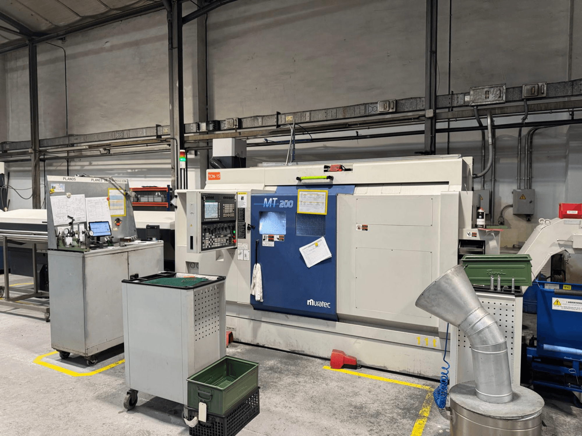 Muratec MT200 meerspillige draaimachine in een fabrieksopstelling, gezien vanaf de voorkant, met bedieningspaneel en omringende apparatuur.