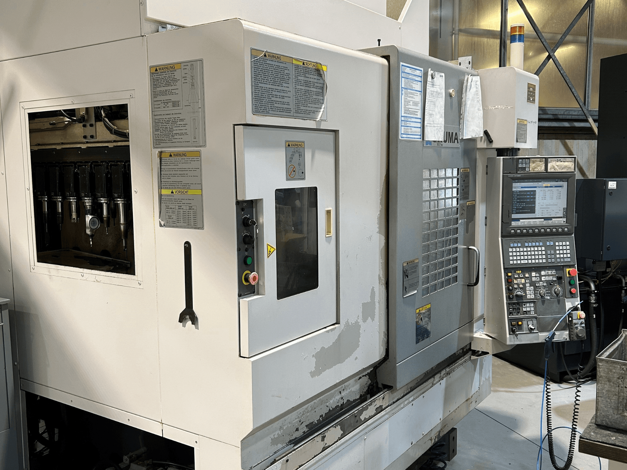 Vooraanzicht van een UMA CNC machine met zichtbare gereedschaphouders, bedieningspaneel, waarschuwingslabels en bedieningsknoppen.