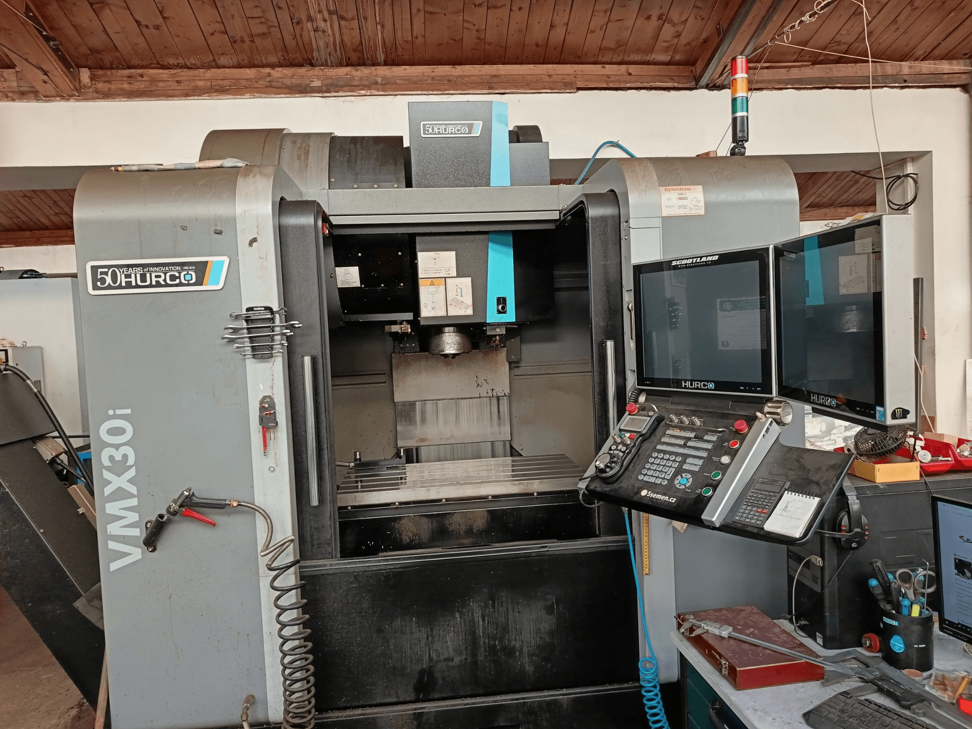 Hurco VMX30i CNC freesmachine in vooraanzicht, met dubbele monitoren, bedieningspaneel en bevestigde slang.