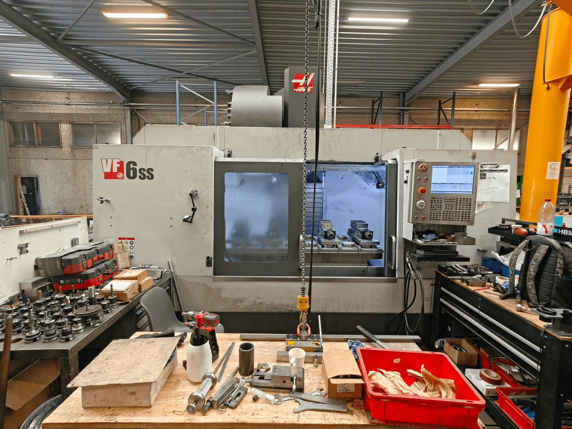 Haas VF-6SS verticaal bewerkingscentrum in een werkplaats, zijaanzicht met het bedieningspaneel en de met gereedschap volgestouwde werkruimte.