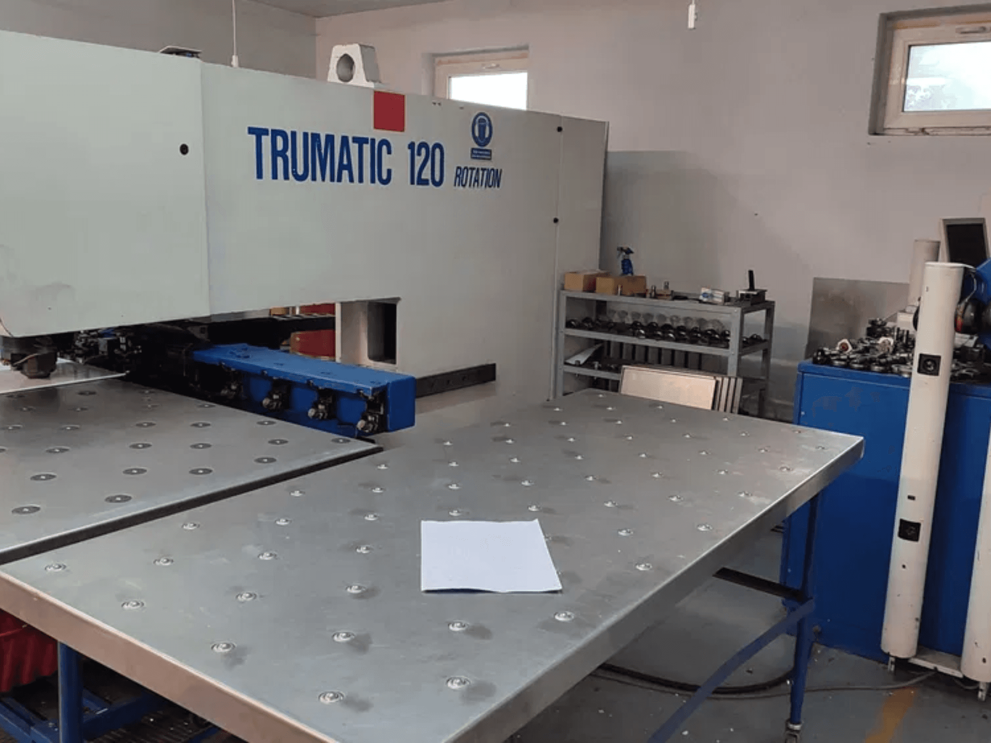 TRUMPF TRUMATIC 120R CNC ponsmachine gezien vanaf de voorkant, met een metalen tafel met geponste gaten en een blanco plaat.