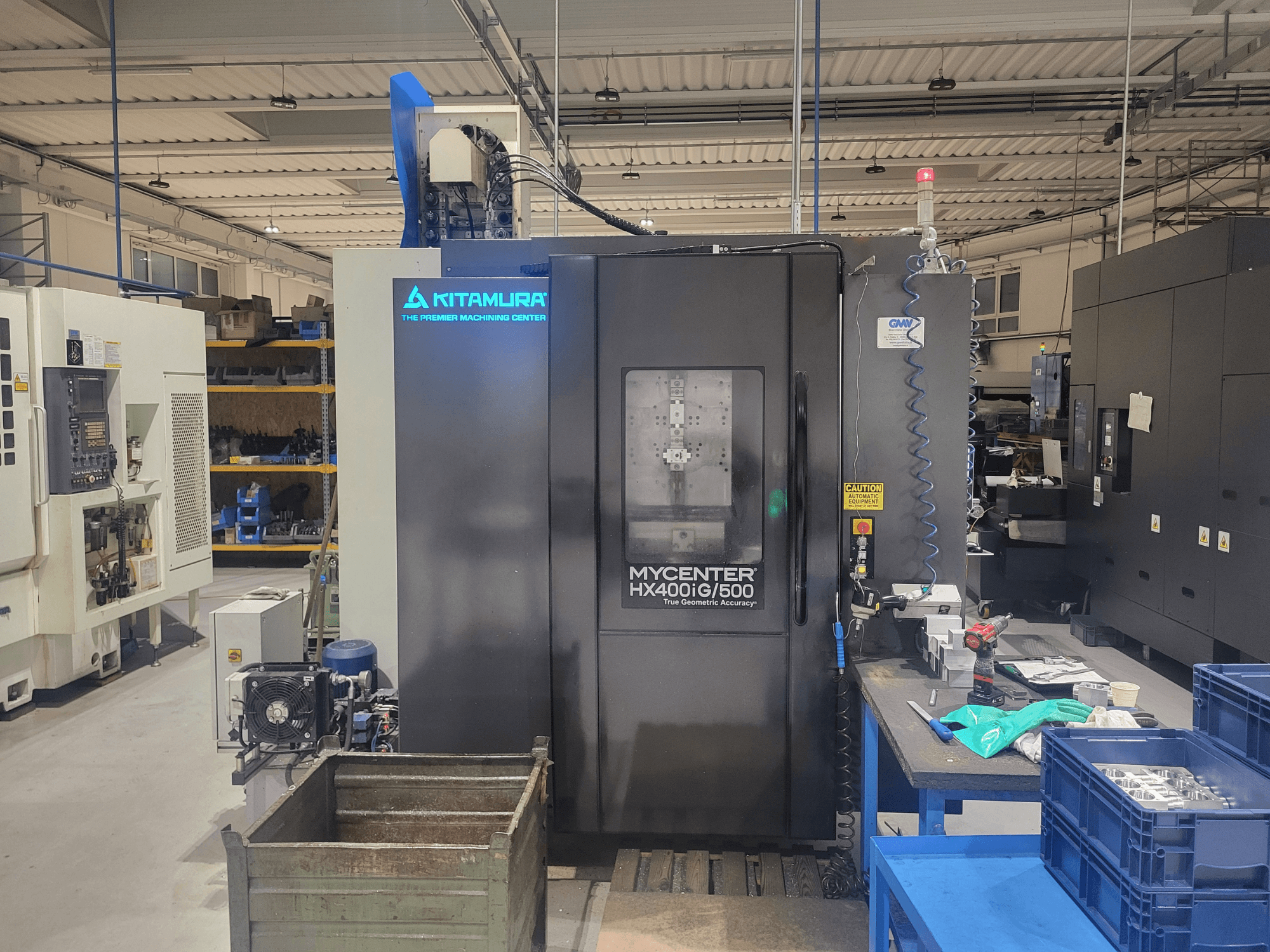 Kitamura Mycenter HX400iG/500 CNC machine in een werkplaats, vooraanzicht, met bedieningselementen, gereedschapopslag en materialen in de buurt.