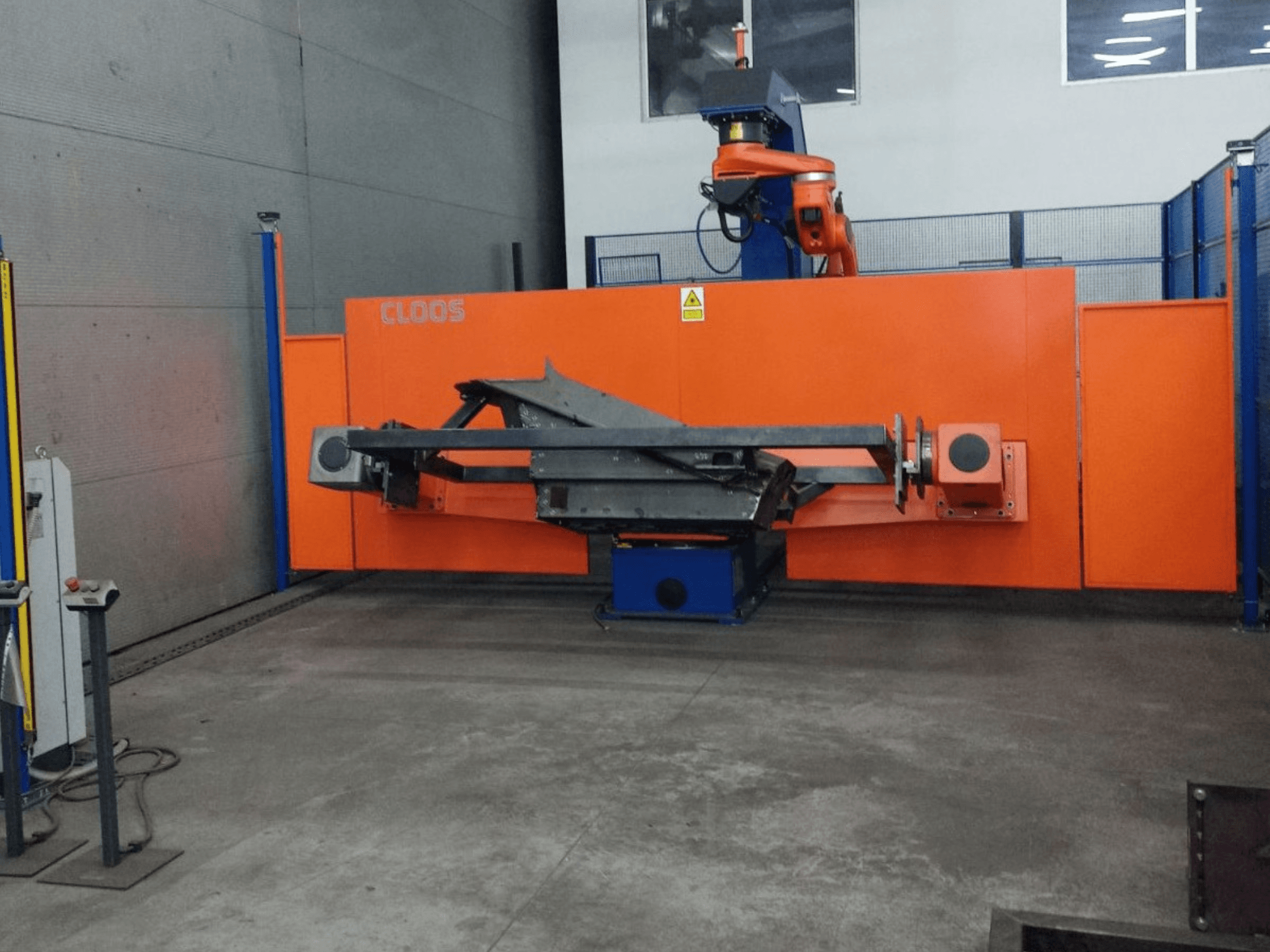 Vooraanzicht van CLOOS QIROX QRC-350-E automatiseringssysteem met robotarm en metaalbewerkingsstructuur in industriële omgeving.