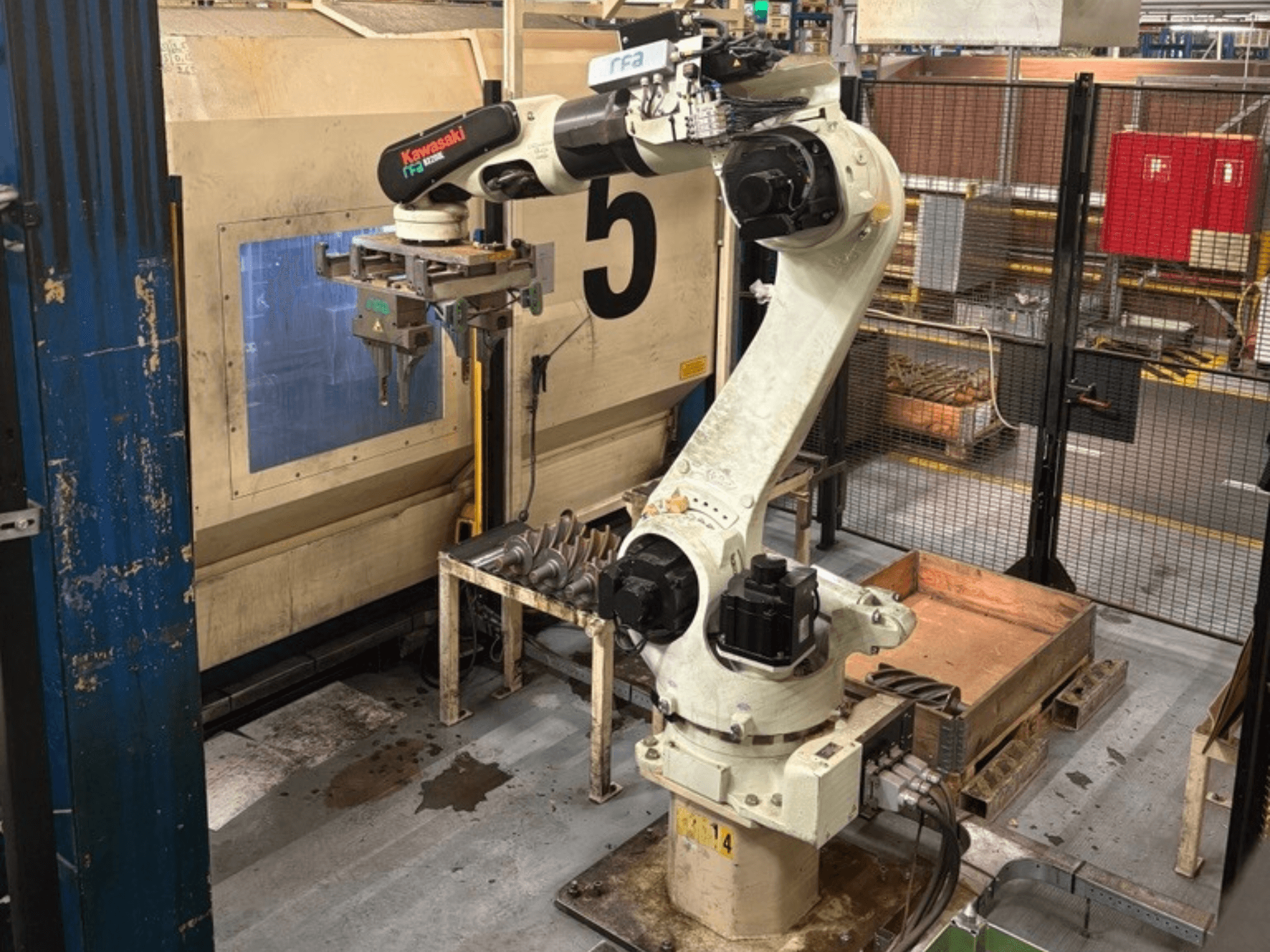 Vooraanzicht van een Kawasaki E42F-A001 robotarm in een industriële omgeving, uitgerust met een grijper en geplaatst bij een werktafel.