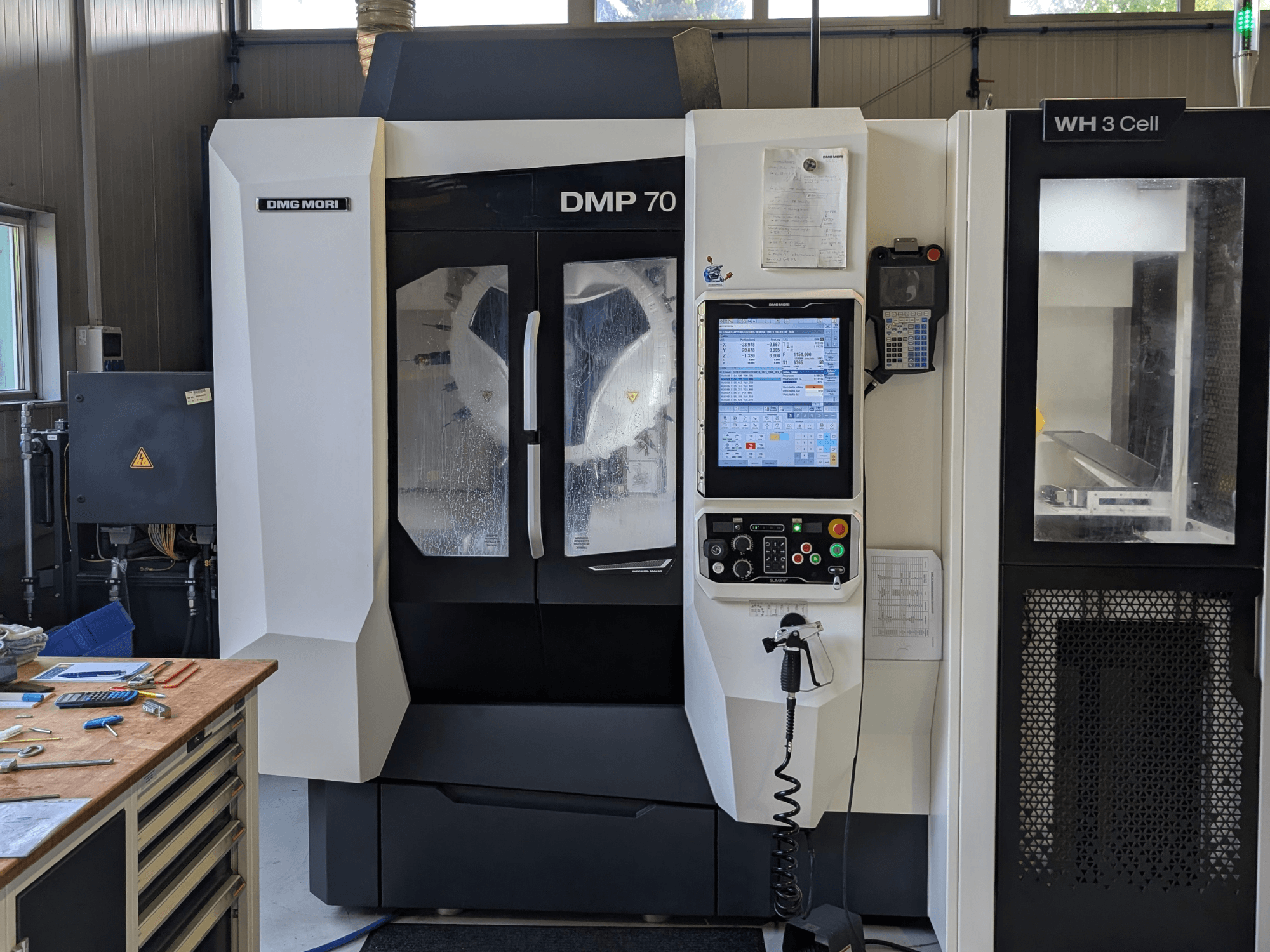 Verticaal bewerkingscentrum DMG MORI DMP 70, vooraanzicht met bedieningspaneel en bedieningsdisplay, omringd door werkplaatsgereedschap.