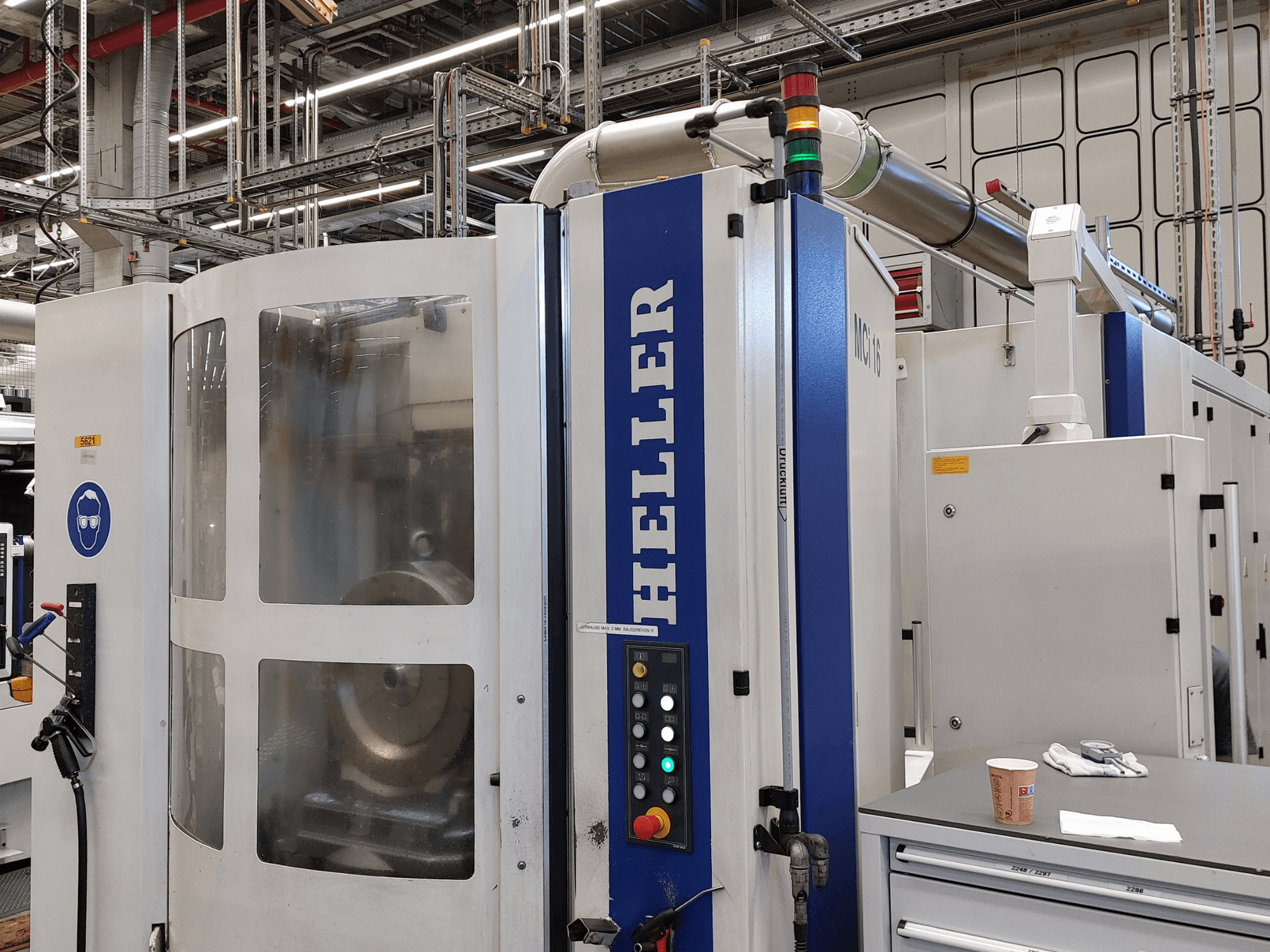Heller MCI 16 verticaal bewerkingscentrum in een fabrieksomgeving, met bedieningspaneel en veiligheidsborden.