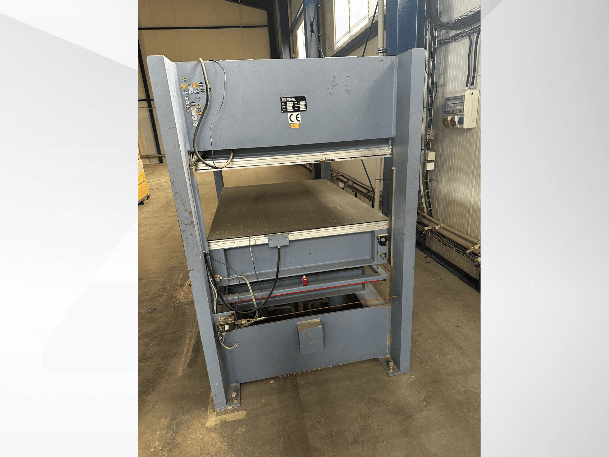 Grijze industriële machine met bedieningspaneel, gezien vanaf de voorkant; bevat verstelbare platforms en veiligheidsmarkeringen.