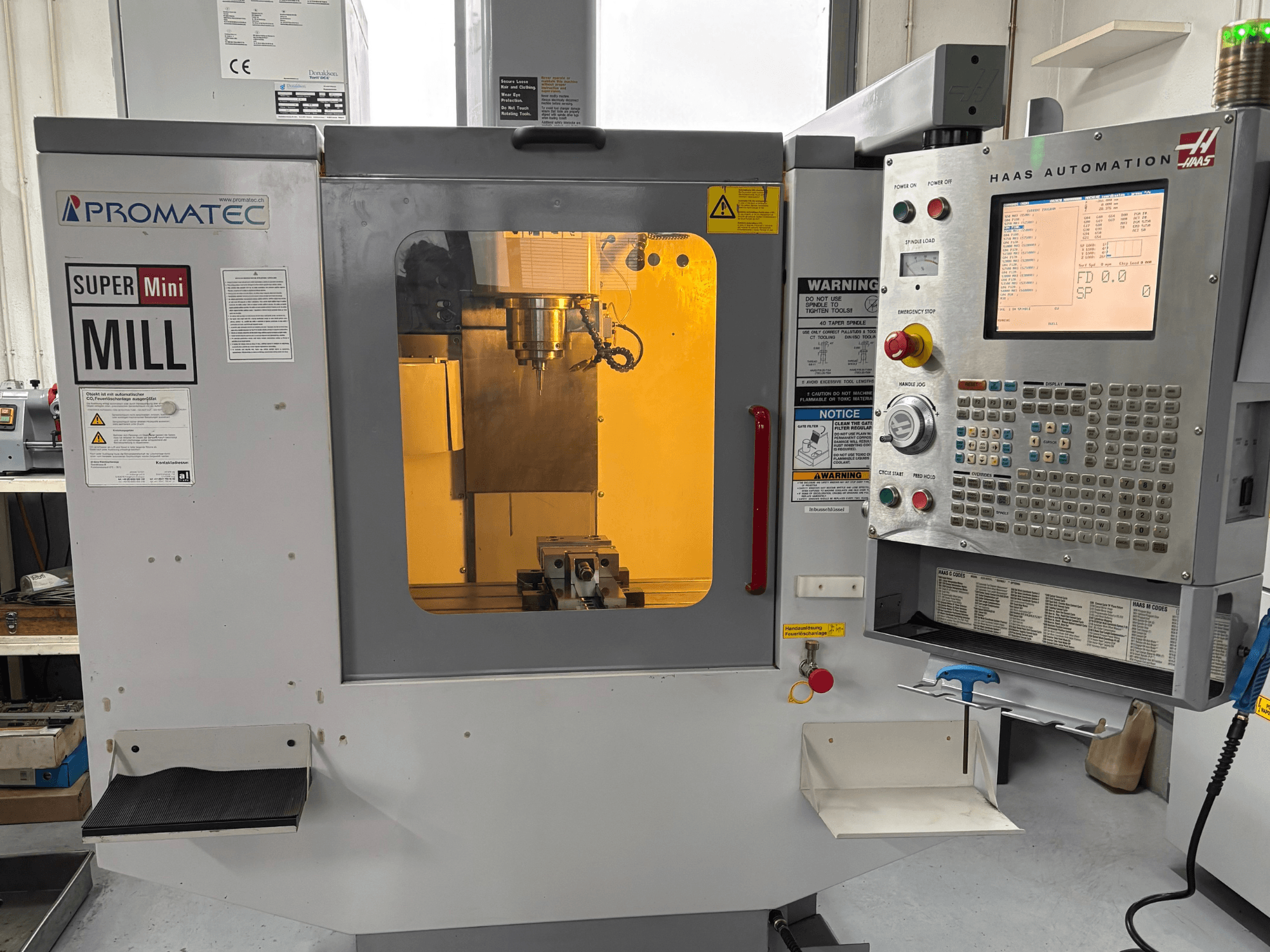 Promatec Super Mini Mill in vooraanzicht, uitgerust met een bedieningspaneel van Haas Automation en zichtbaar snijgereedschap binnenin.