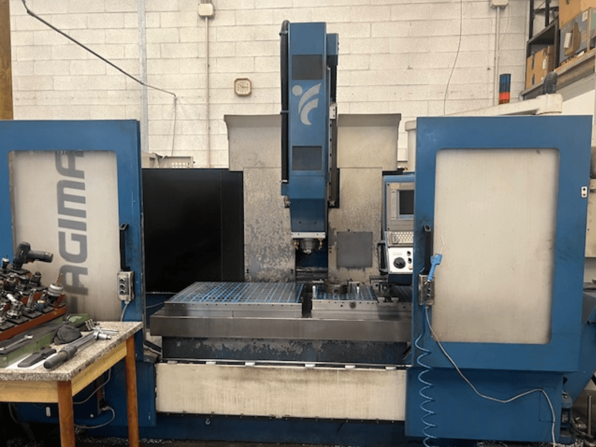 Een vooraanzicht van een JAGIMA CNC machine met een groot metalen werkblad, zichtbaar bedieningspaneel en gereedschappen op een nabijgelegen tafel.