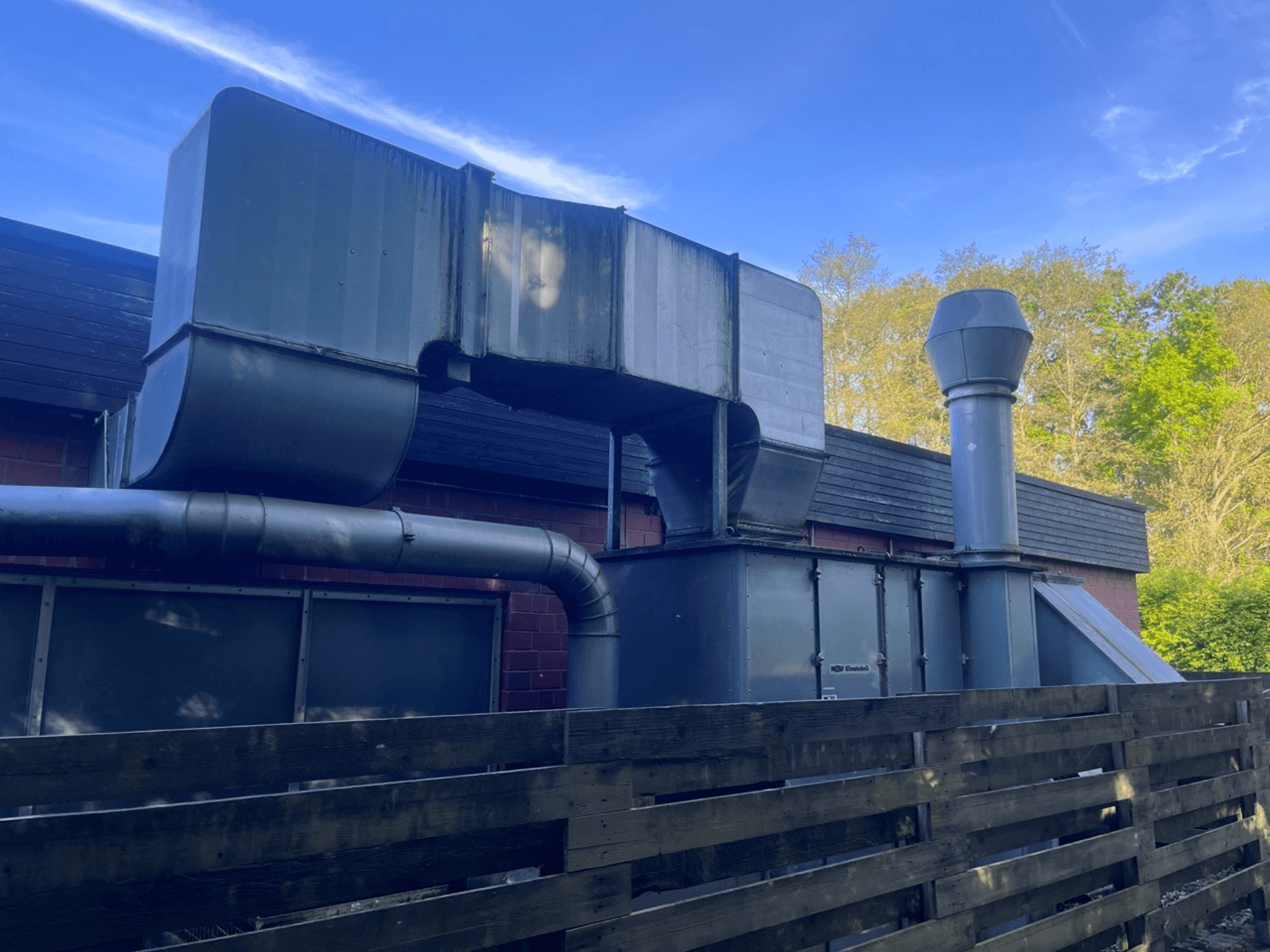 Industrieel ventilatiesysteem met metalen kanalen, zijaanzicht; omvat een vierkante en cilindrische schoorsteen, groene afwerking.