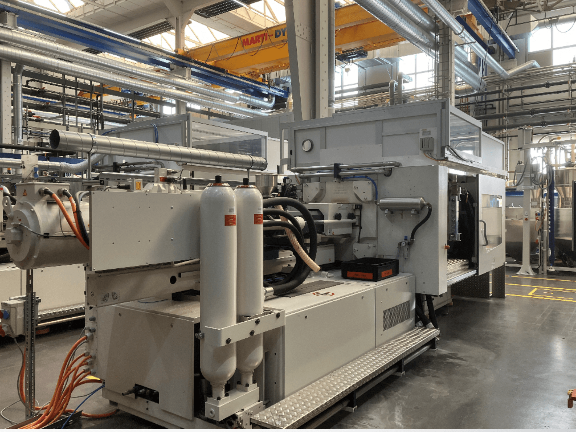 Industriële machine getoond in zijaanzicht met meerdere slangen, twee verticale tanks en bedieningspaneel; merk/model niet zichtbaar.