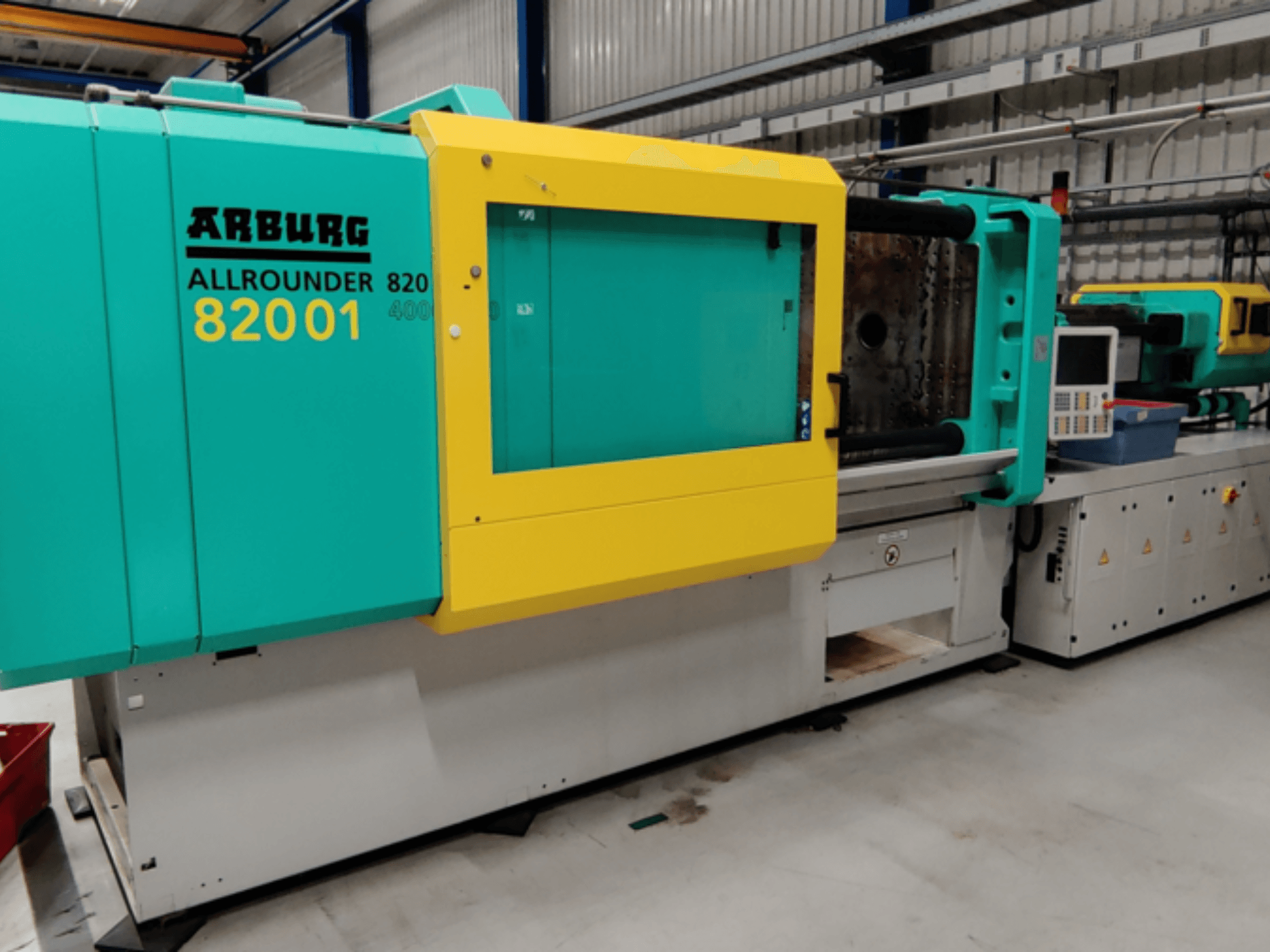 Arburg ALLROUNDER 82001 spuitgietmachine in groenblauw en geel, zijaanzicht van het bedieningspaneel en de bedieningsfuncties.