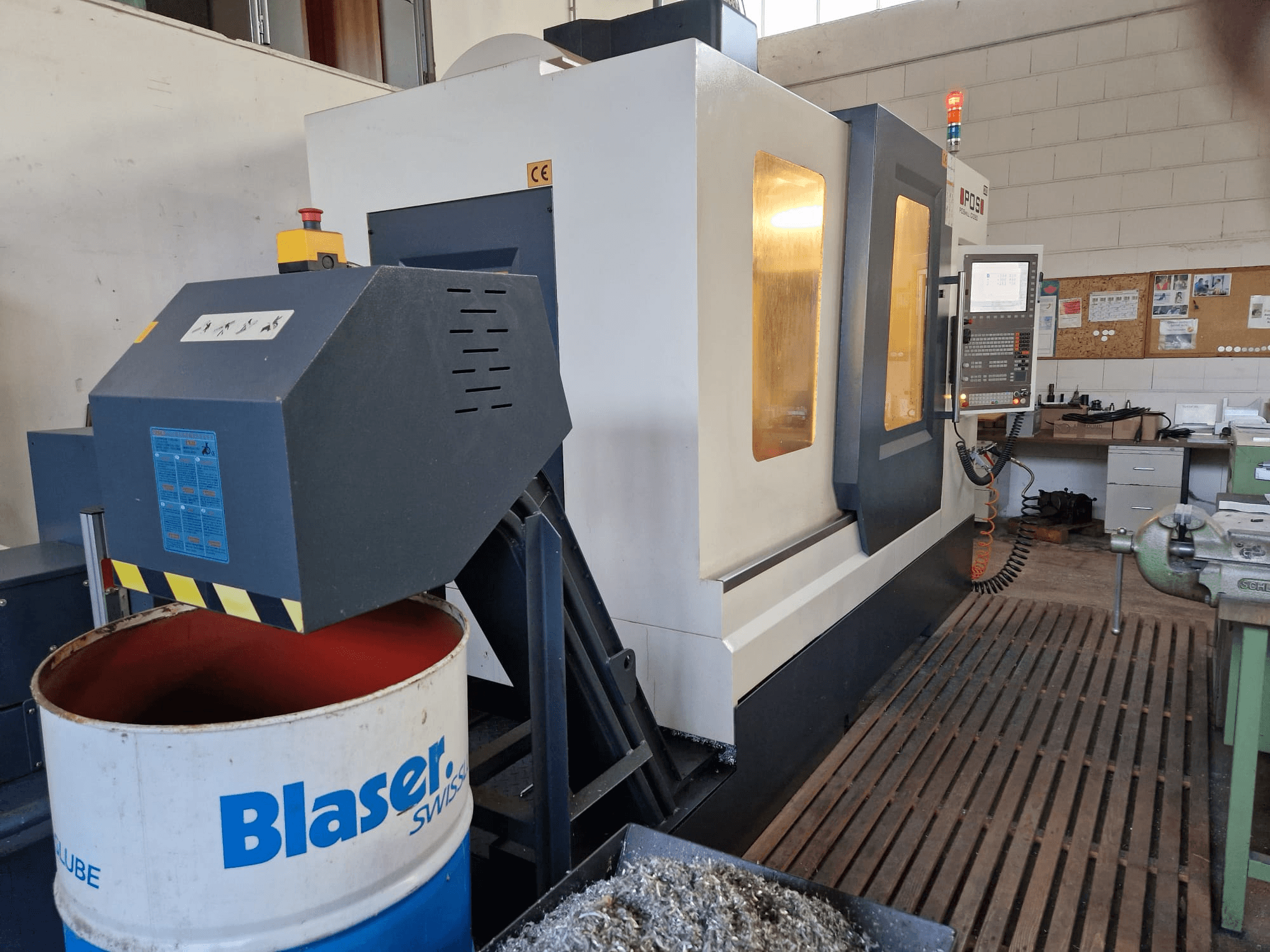 Vooraanzicht van POSmill C 1050 verticaal bewerkingscentrum, met koelvloeistofsysteem boven Blaser-trommel en bedieningspaneel zichtbaar.