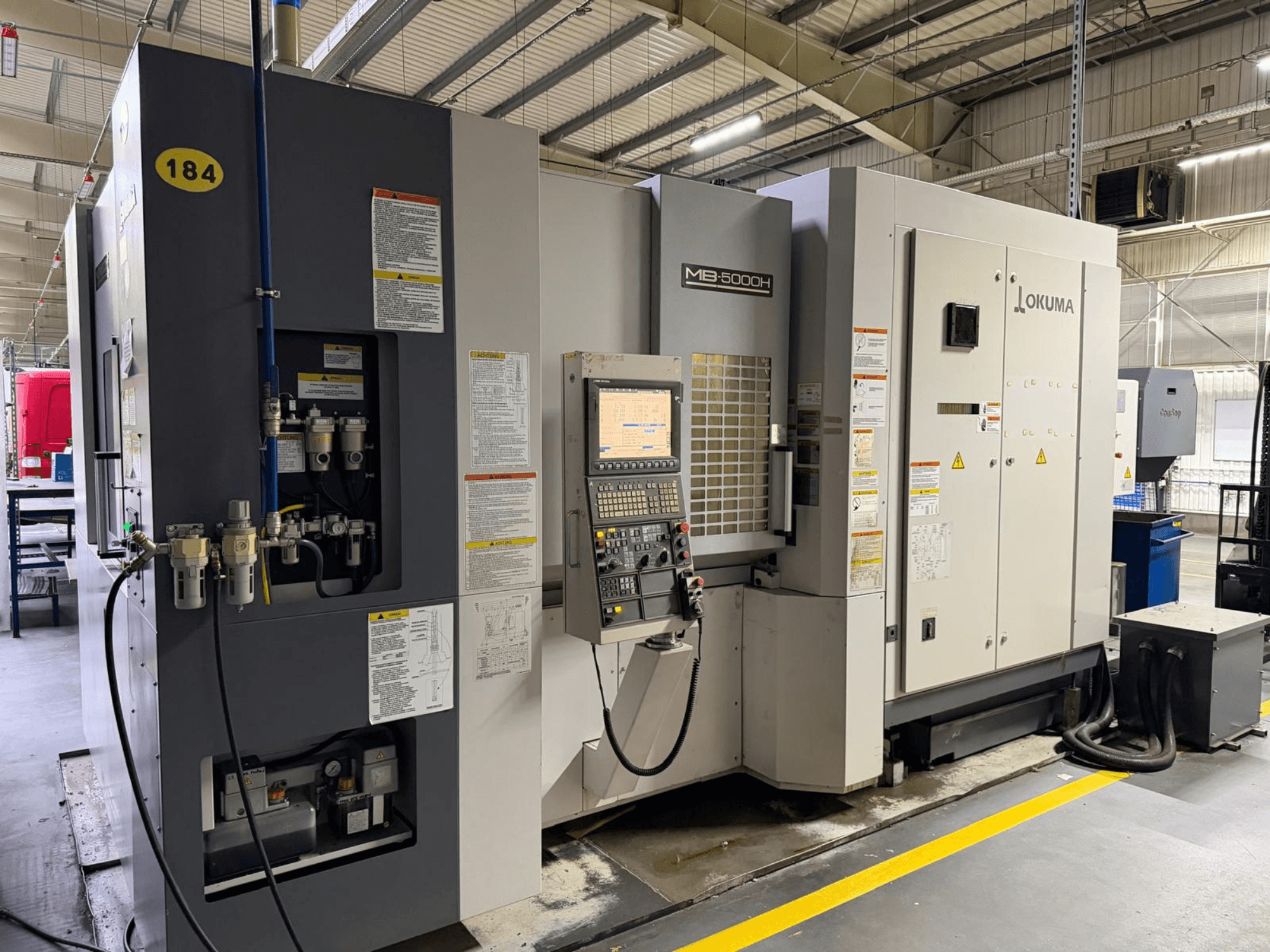 Okuma MB 5000H horizontaal bewerkingscentrum vooraanzicht, met bedieningselementen, labels en hydraulische aansluitingen.