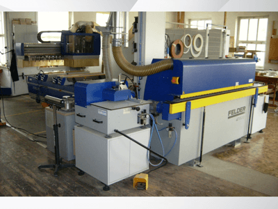 FELDER G500-kantenlijmmachine in een werkplaats, zijaanzicht van de blauw-gele constructie met bedieningselementen en afzuigkanalen.