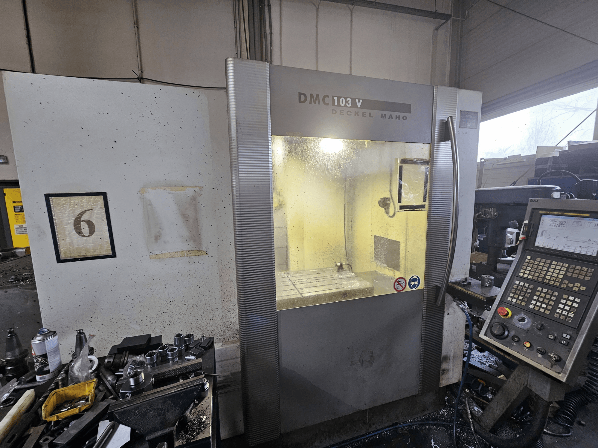 Vooraanzicht van een Deckel Maho DMC 103 V CNC machine, met het bedieningspaneel, het werkgebied en de genummerde indicator "6".