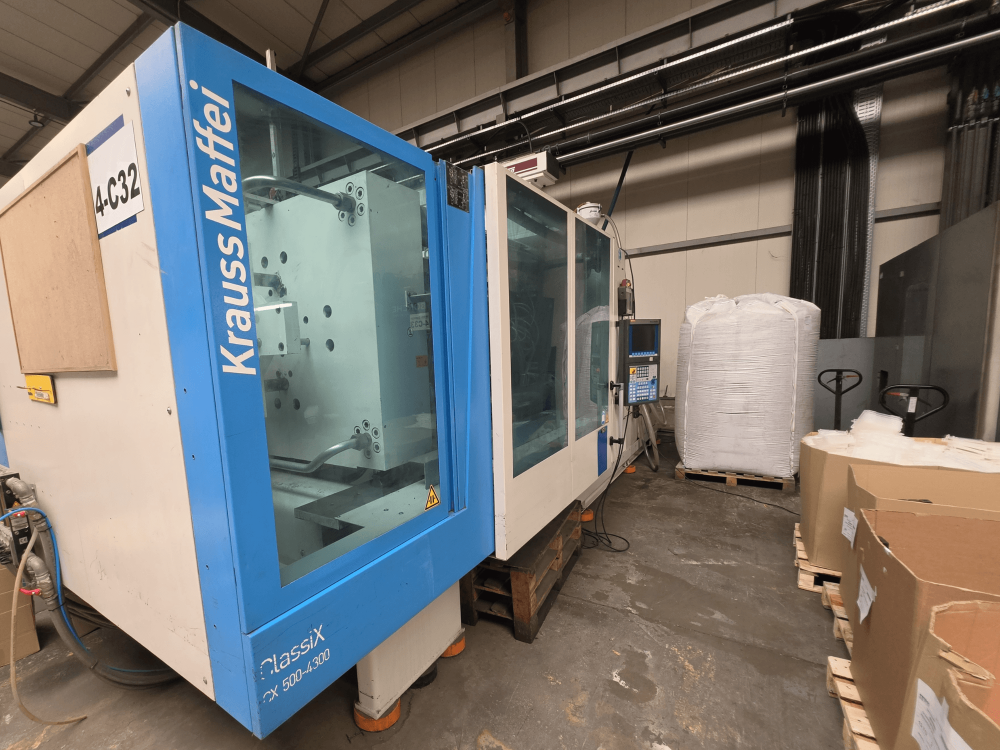 Krauss Maffei 500-4000 CX hydraulische spuitgietmachine, zijaanzicht, met het bedieningspaneel en nabijgelegen verpakkingsmaterialen.