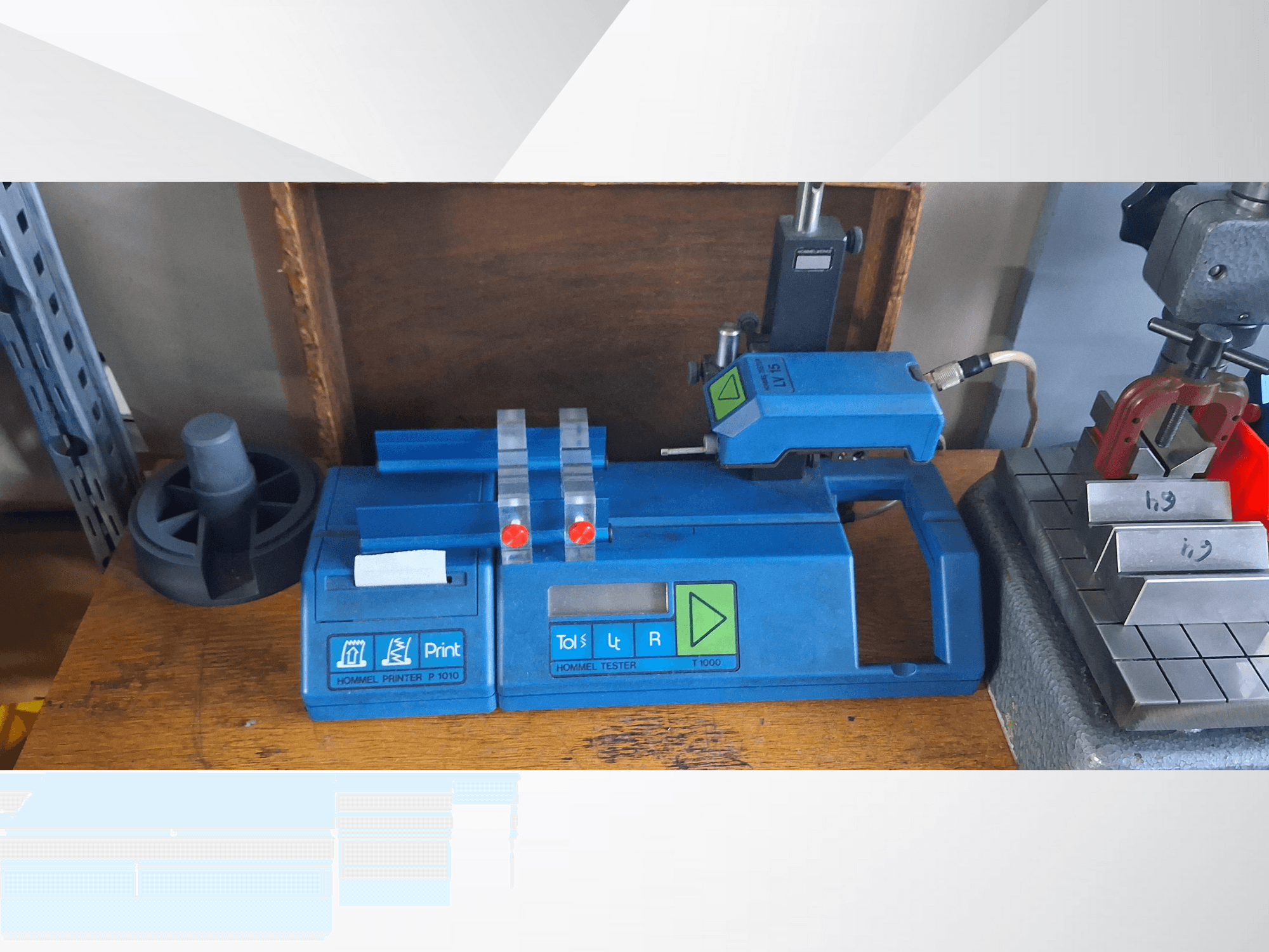 Blauwe Hommel T 1000 printer en T 1 010 tester met rode knoppen, gezien vanaf de voorkant op een werkbank met metalen blokken.