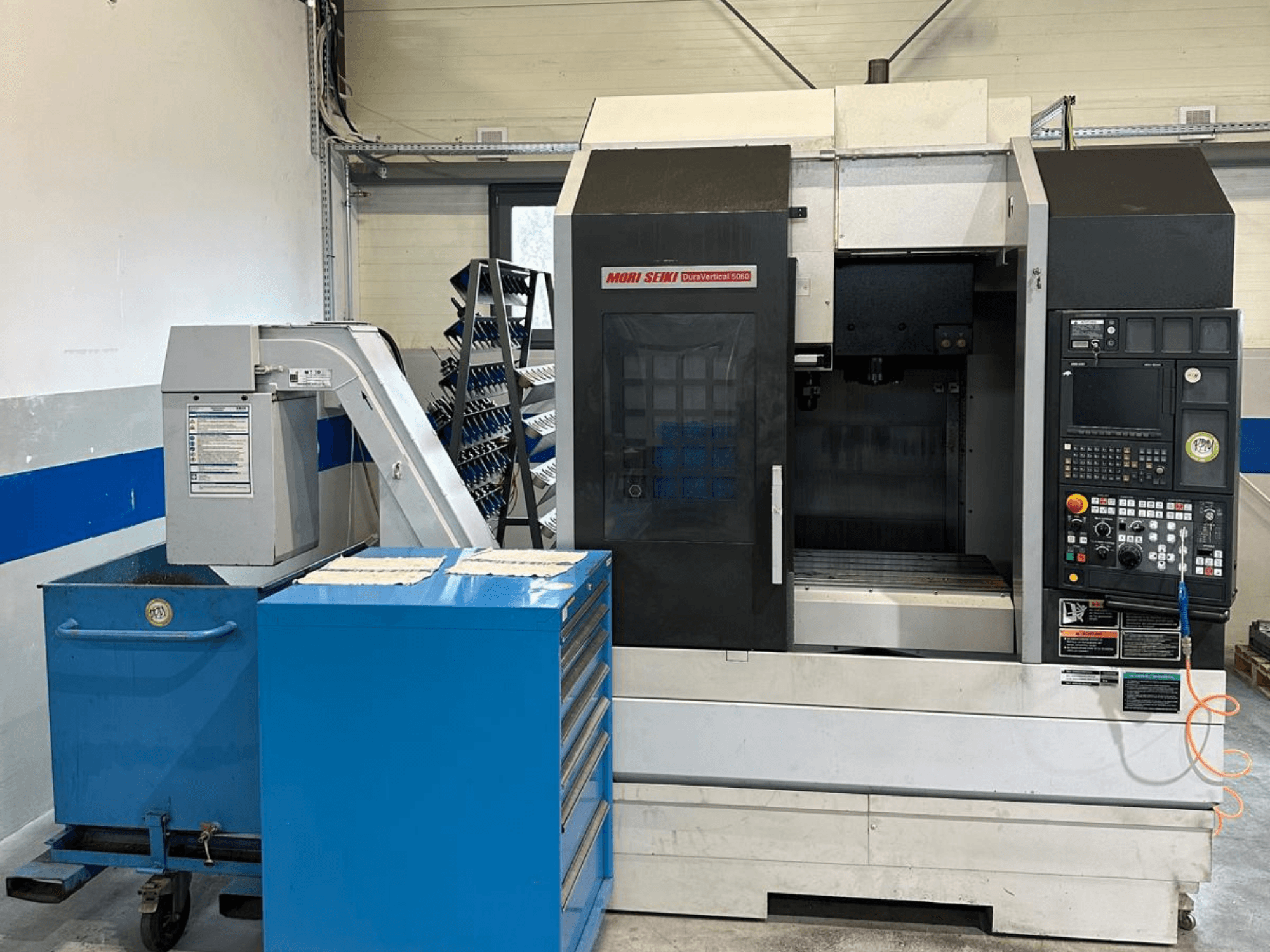 MORI SEIKI DURA VERTICAL 5060, vooraanzicht van een verticaal bewerkingscentrum met bedieningspaneel en een nabijgelegen gereedschapopslag.