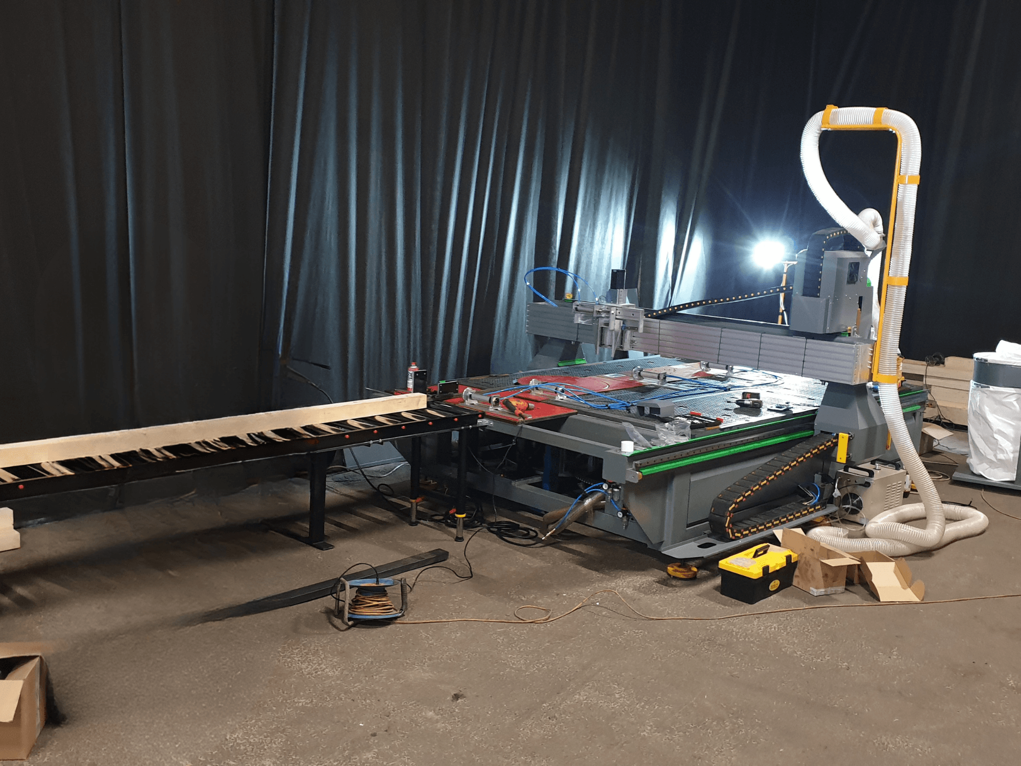 CNC machine met een zijtransportband, gereedschap op de tafel en kanaal voor stofopvang. Zwarte achtergrond, vooraanzicht.