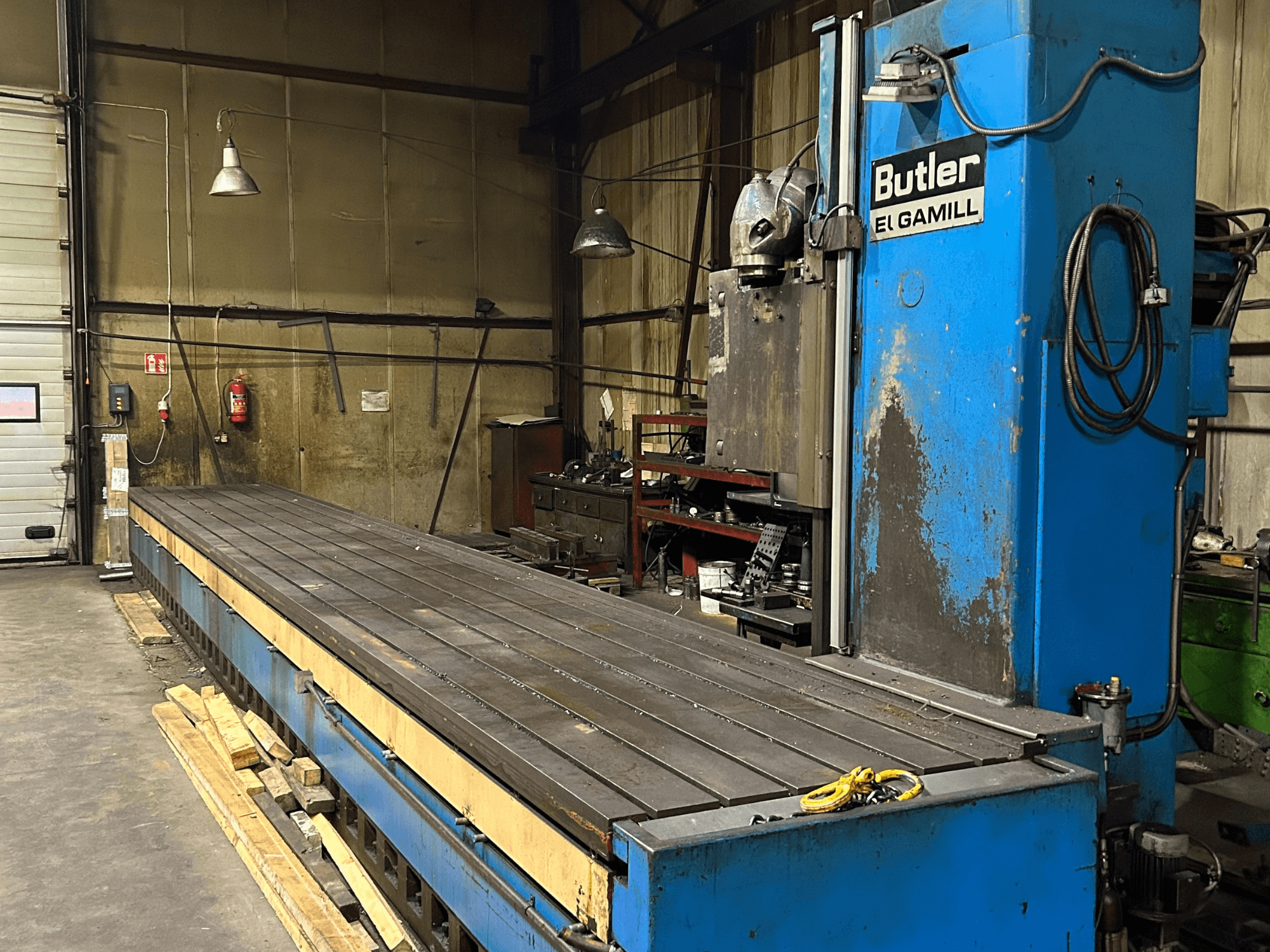 Blauwe Butler El Gamill freesmachine in een werkplaats, zijaanzicht met een lange vlakke tafel en bedieningselementen rechts.