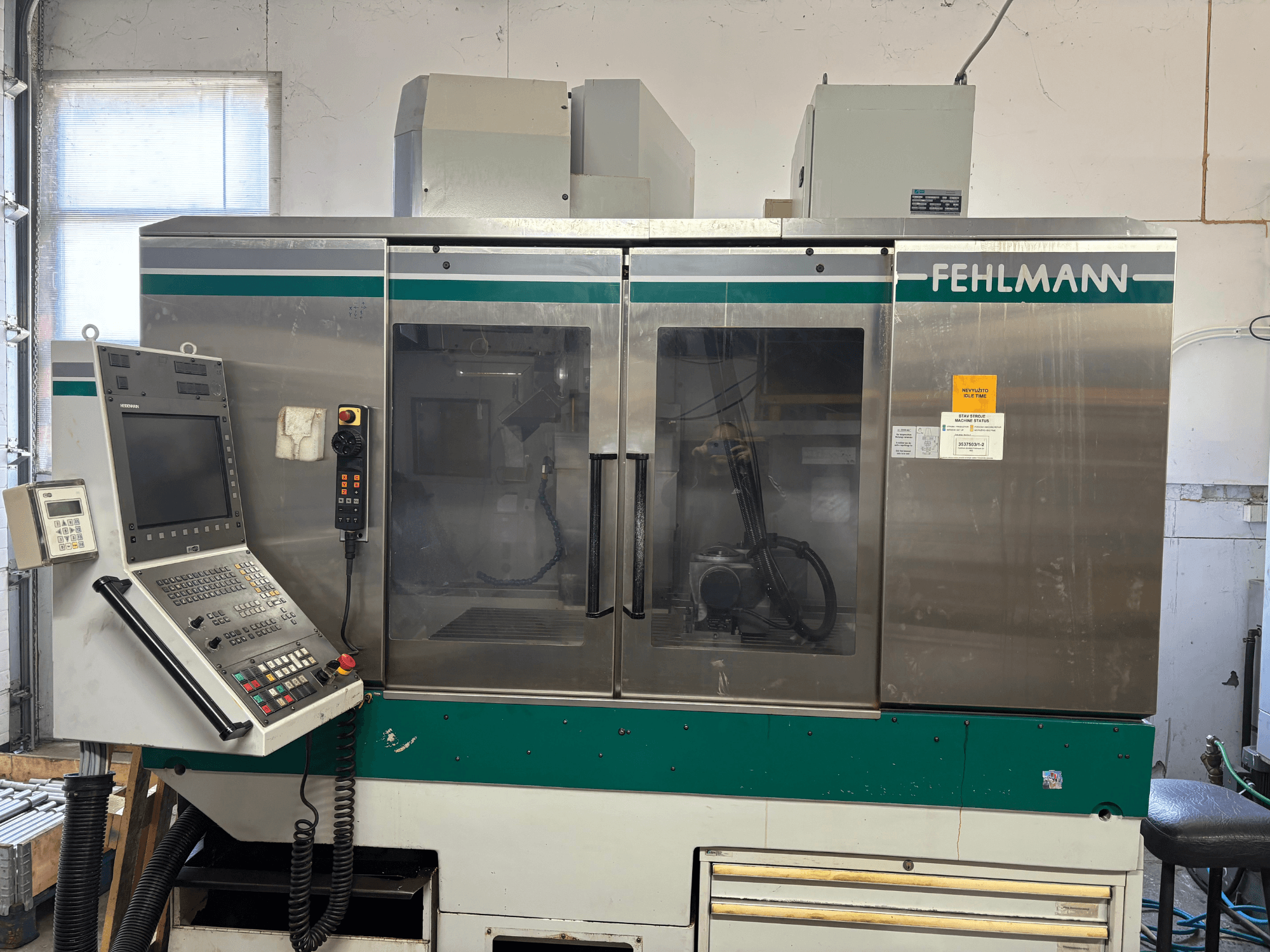 Vooraanzicht van het verticale bewerkingscentrum FEHLMANN Picomax 90-M, met bedieningspaneel, doorzichtige behuizing en bedieningsknoppen.