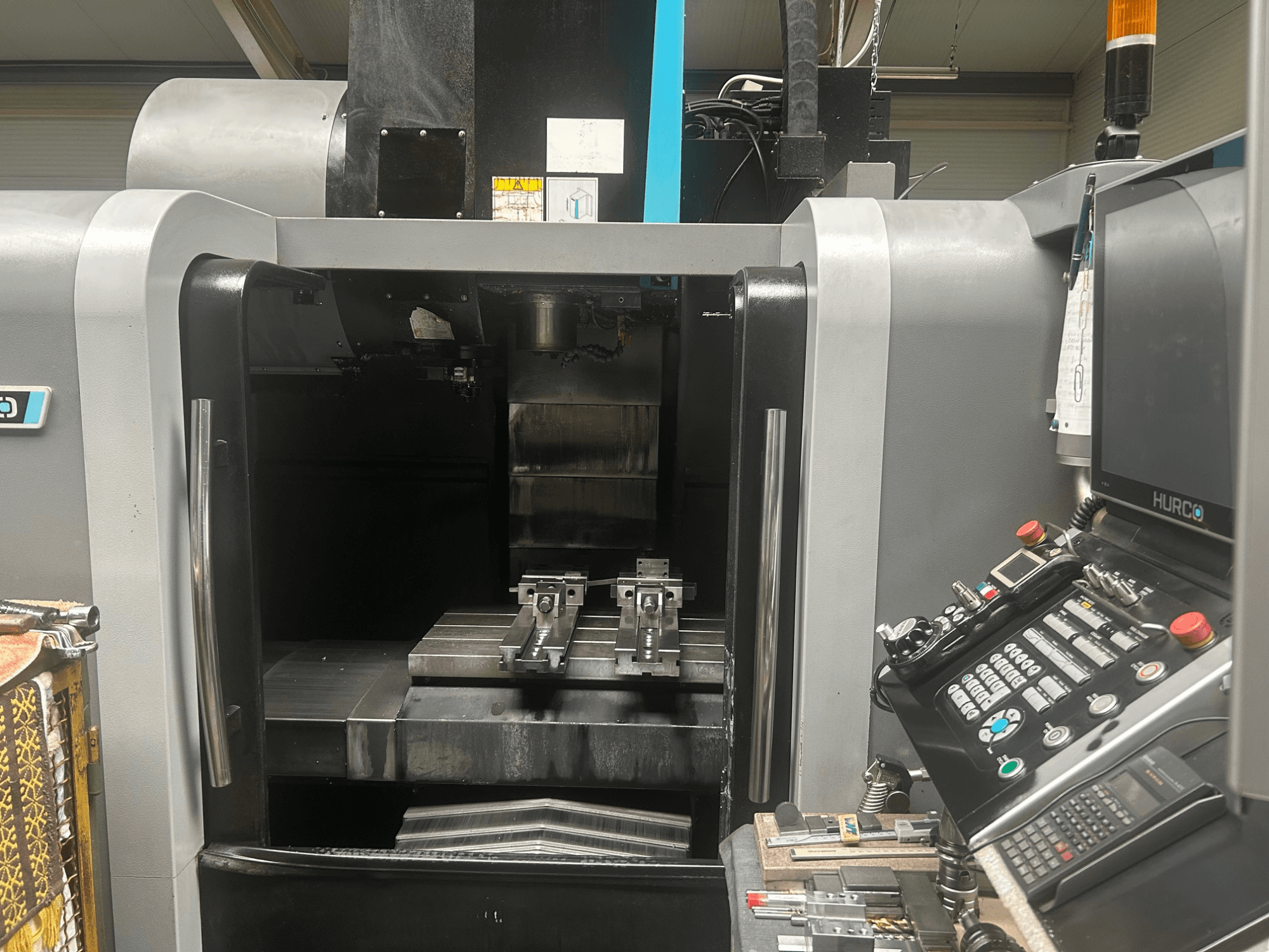 Vooraanzicht Hurco CNC bewerkingscentrum, met gereedschaphouder, metalen werkstuk en bedieningspaneel met knoppen en display.