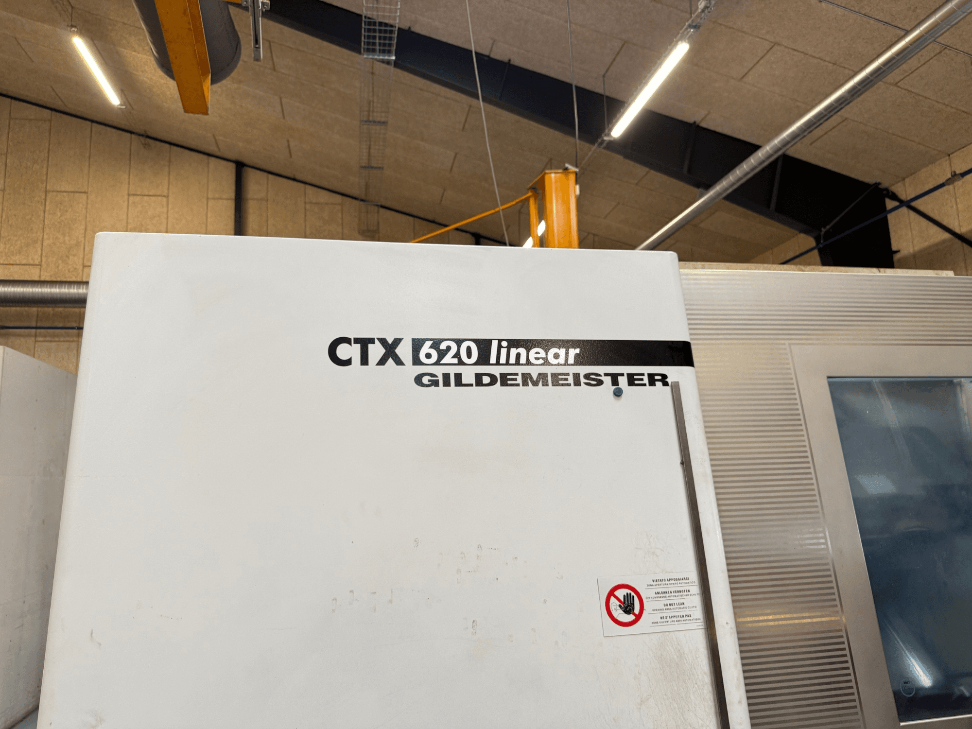 Zijaanzicht CTX 620 lineaire Gildemeister machine, met een witte buitenkant en veiligheidswaarschuwingslabels.