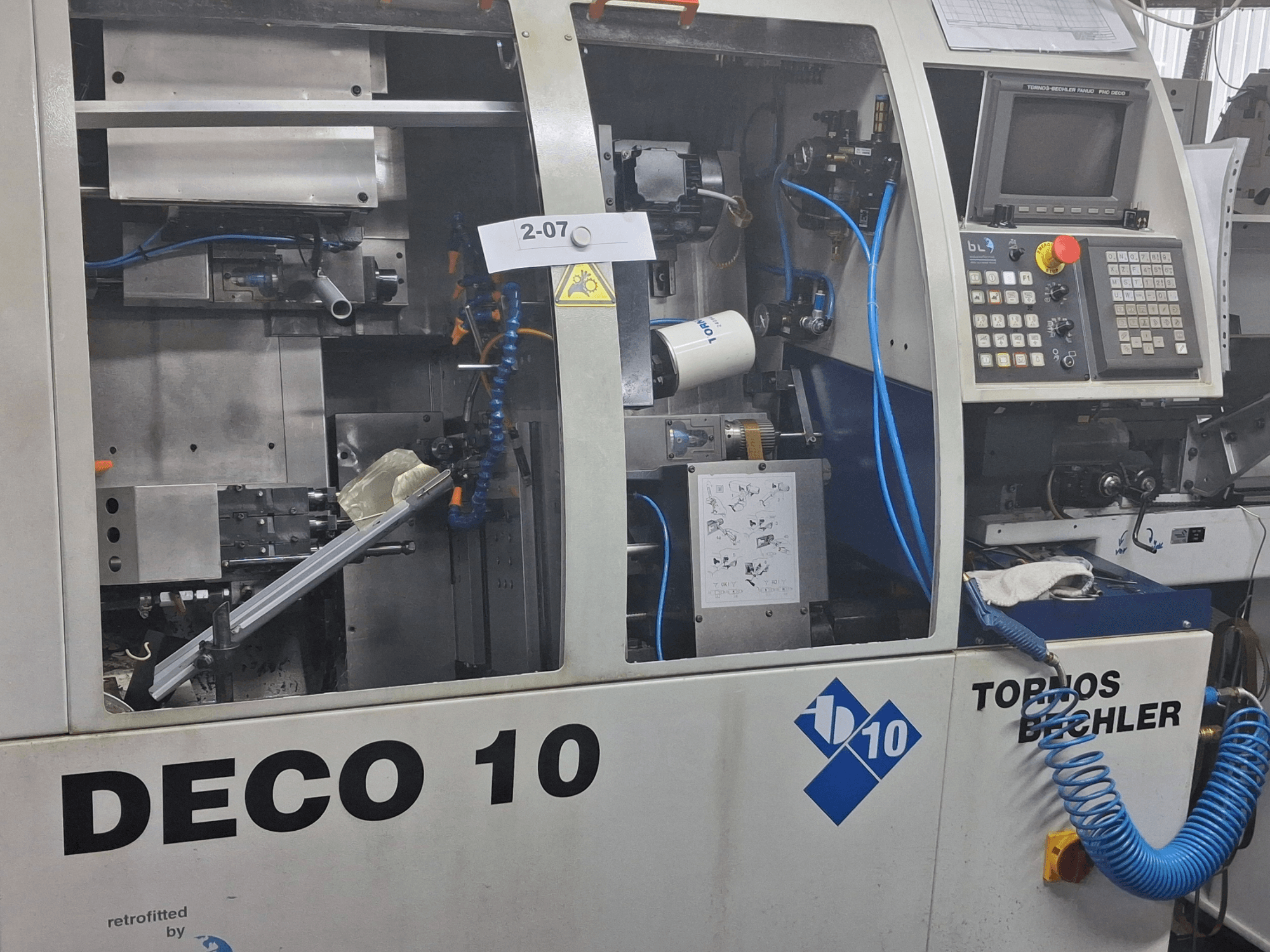 Close-up van de TORNOS Deco 10a Zwitserse draaimachine, met details van het interne mechanisme en bedieningspaneel.