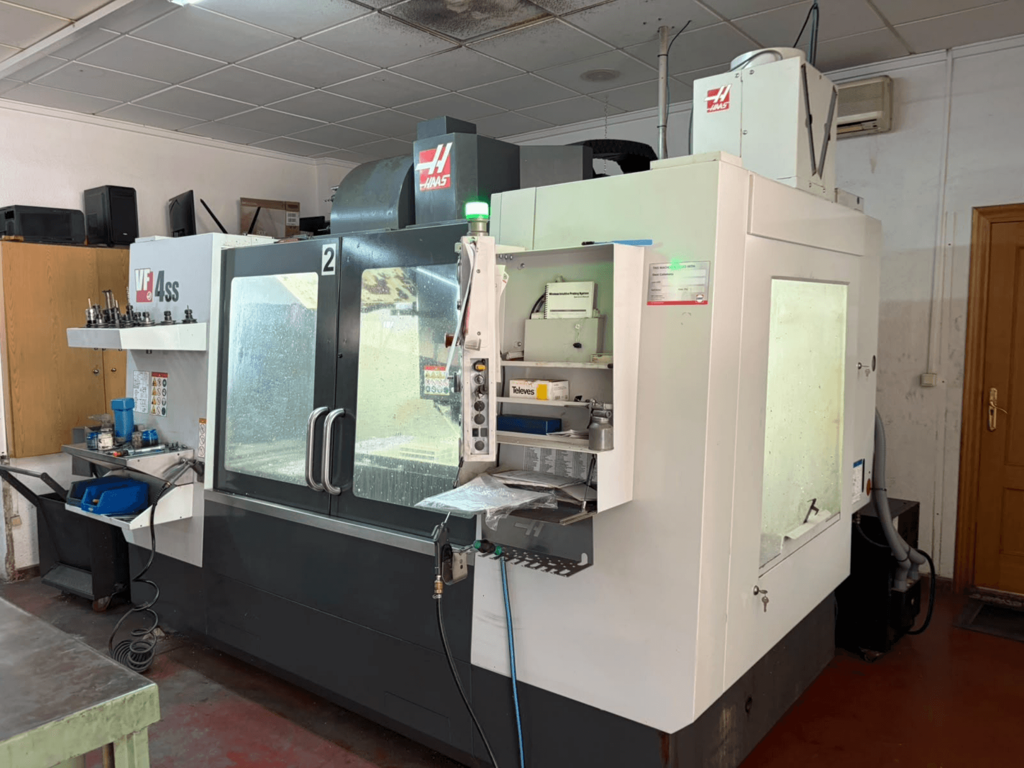 HAAS VF 4SS verticaal bewerkingscentrum in een werkplaats, vooraanzicht, met het bedieningspaneel en de werkruimte met gereedschappen en materialen.