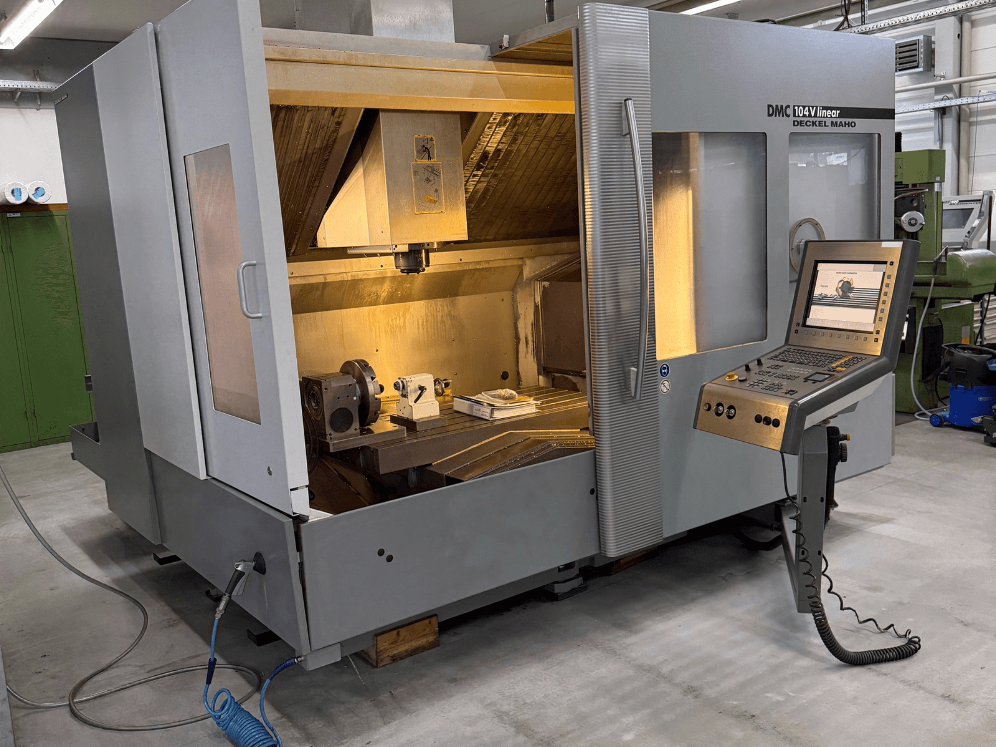 DMC 104 V lineair verticaal bewerkingscentrum in een werkplaats, met het bedieningspaneel en de gedeeltelijk open behuizing.
