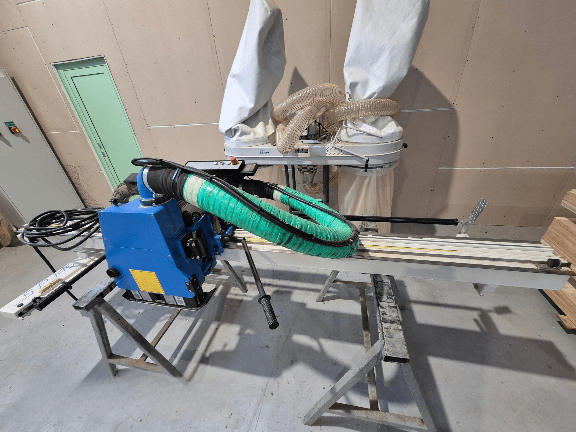 Blauwe SVP-175 horizontale paneelzaag met groene stofslang en steun, gezien vanaf de zijkant in een werkplaats.