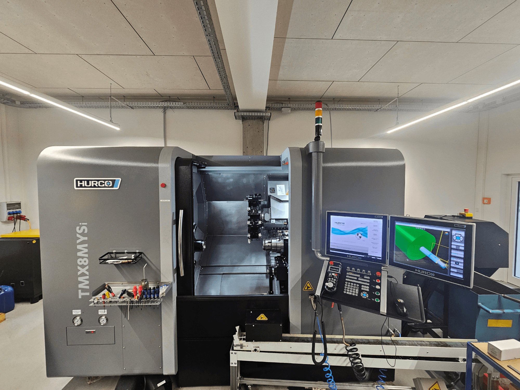 Hurco TMX 8 MYSi draaifreescentrum in een werkplaats, met dubbele monitoren, bedieningspaneel en gereedschappen aan de zijkant.