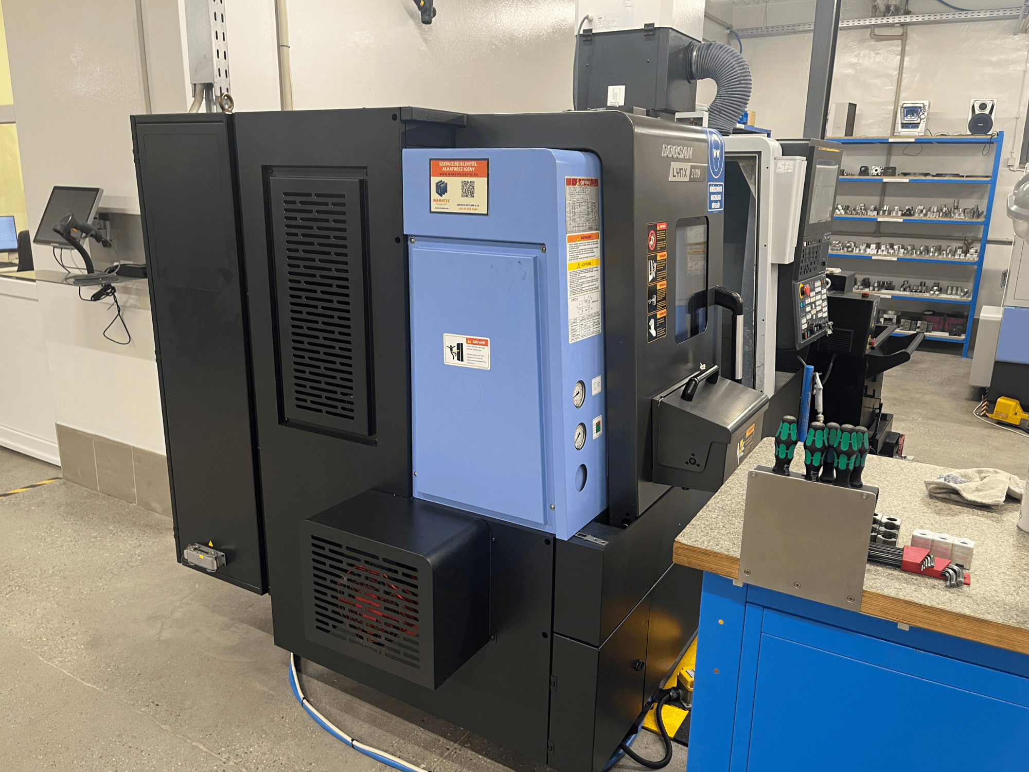 Doosan Lynx 2100 draaibank, zijaanzicht, met het bedieningspaneel, ventilatiesysteem en gereedschap op een werkbank.