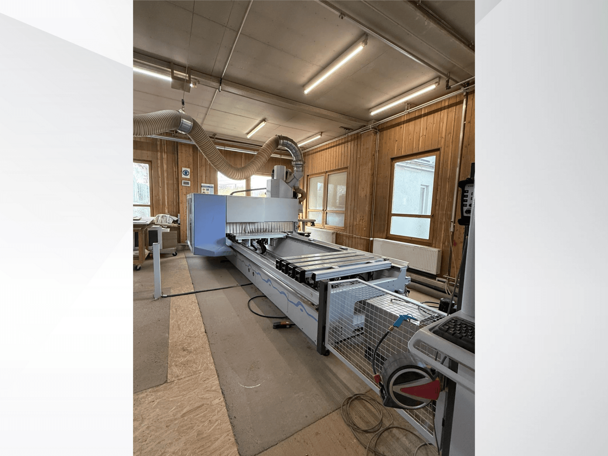 CNC freesmachine in een werkplaats, zijaanzicht, met een grote blauwe behuizing, aangesloten transportband en zichtbaar bedieningspaneel.