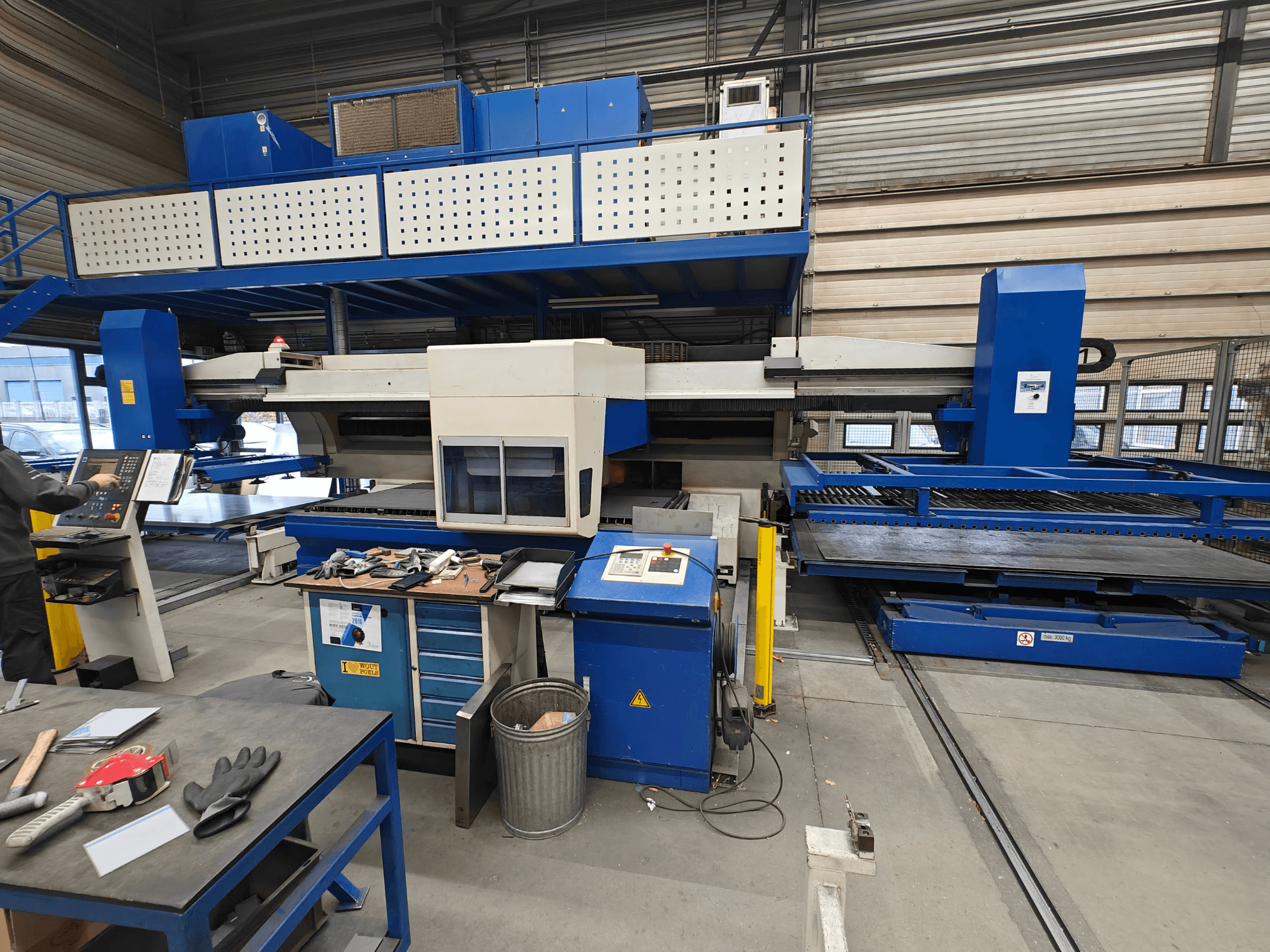 Industriële CNC machine vanuit vooraanzicht, met blauw-witte constructie, bedieningspaneel en verschillende gereedschappen op de werktafel.