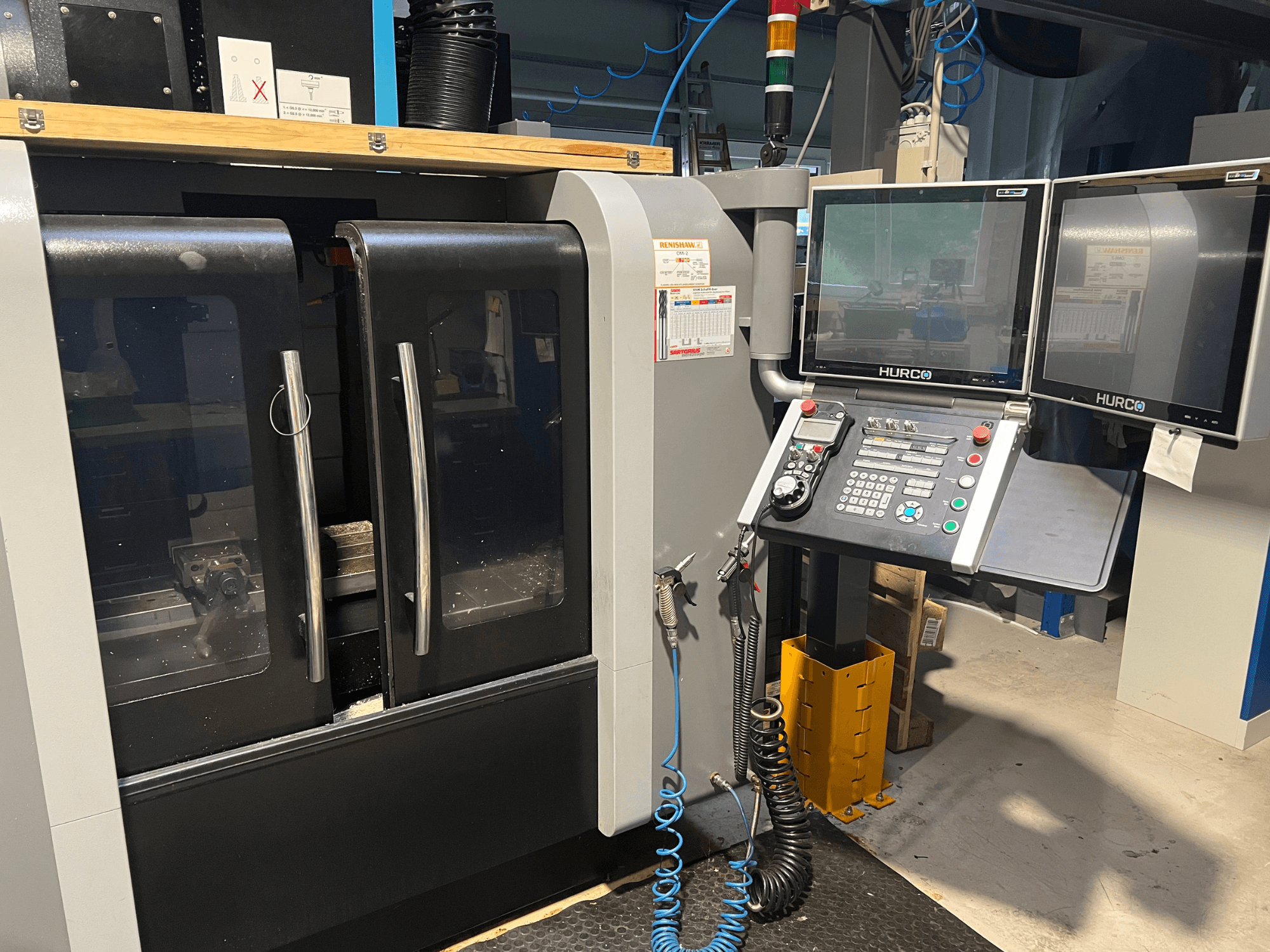Vooraanzicht Hurco CNC machine met dubbele monitoren en bedieningspaneel. Voorzien van doorzichtige deuren en zichtbaar bewerkingsgebied binnenin.