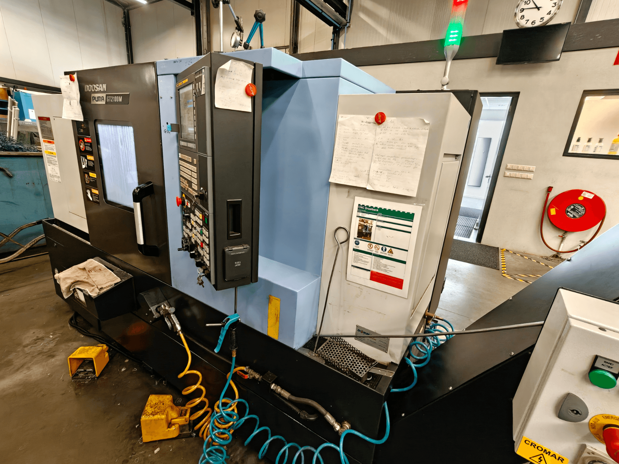 Vooraanzicht van de DOOSAN Puma GT 2100M horizontale draaimachine met het bedieningspaneel, de veiligheidsvoorzieningen en onderhoudsinstructies zichtbaar.