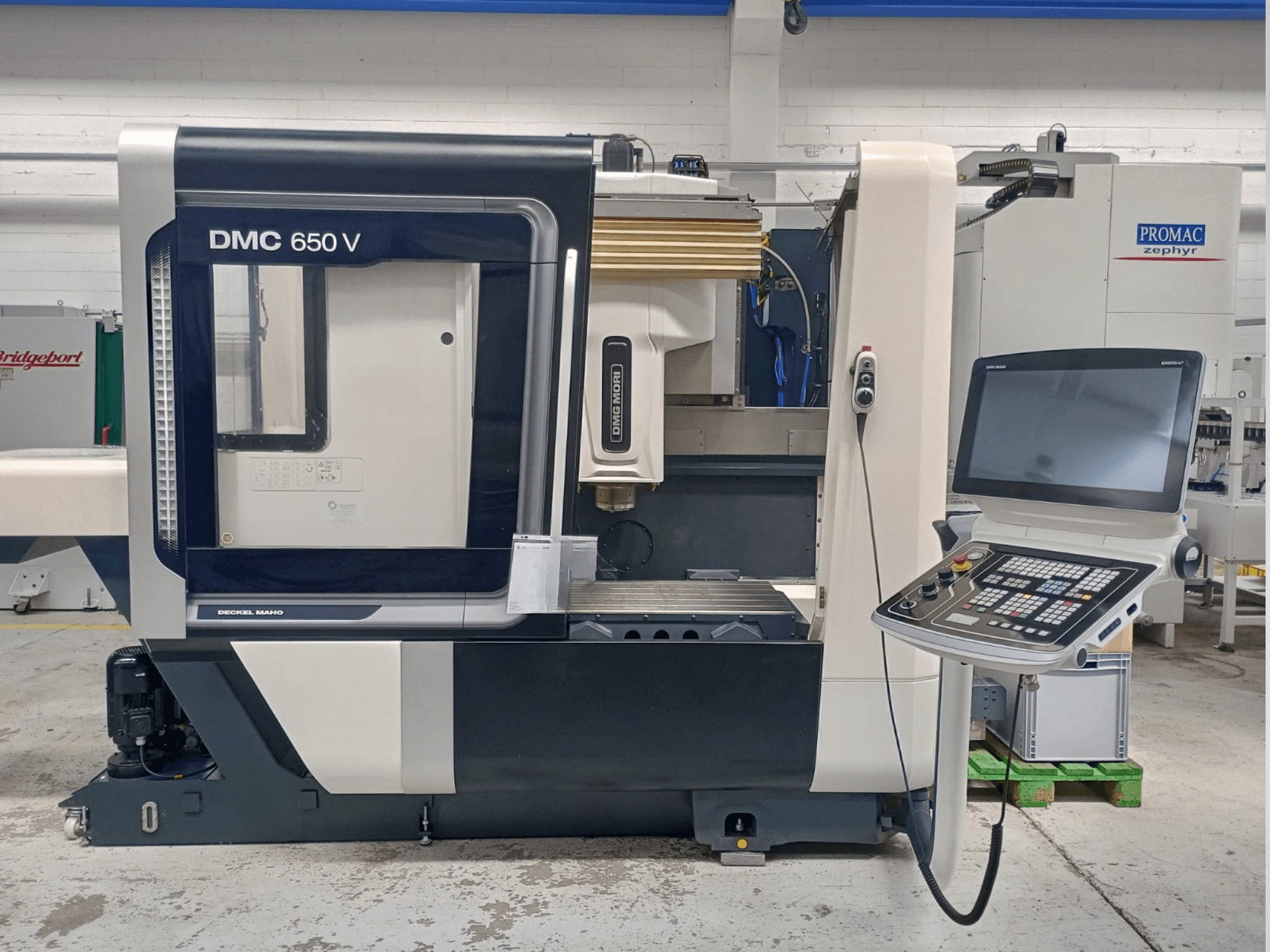 Decker Maho DMC 650 V CNC machine zijaanzicht, met een bedieningspaneel met knoppen en een scherm, in een industriële omgeving.