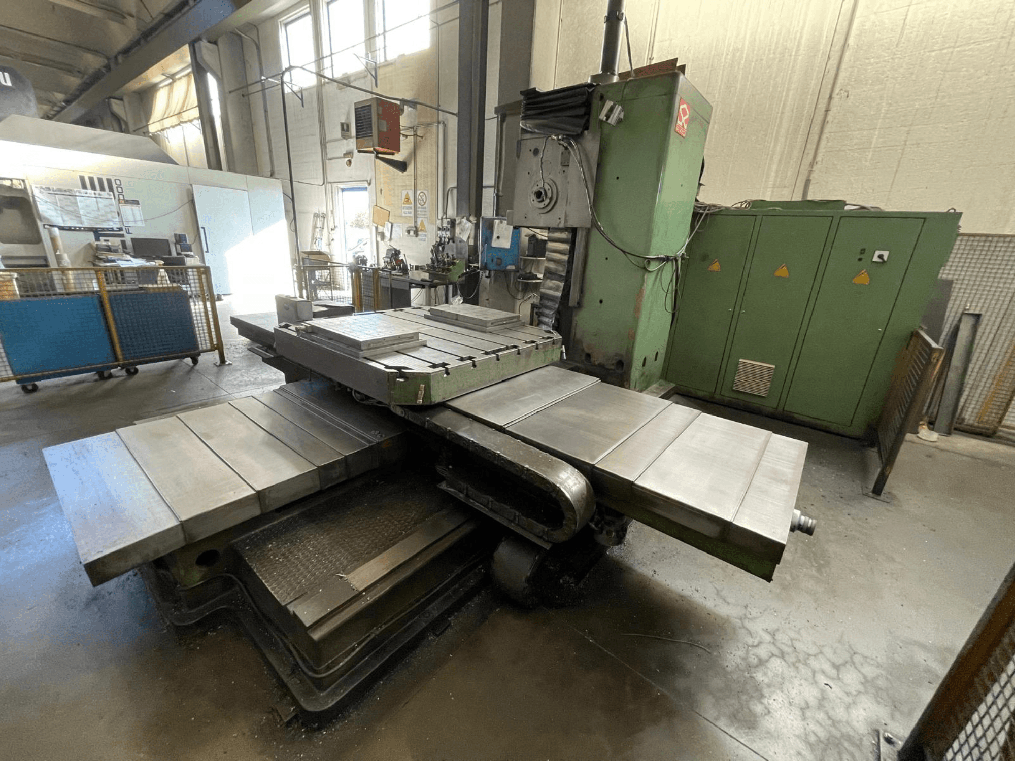 Grote industriële freesmachine met groene behuizing, zijaanzicht, met meerdere vlakke oppervlakken en opbergkasten op de achtergrond.