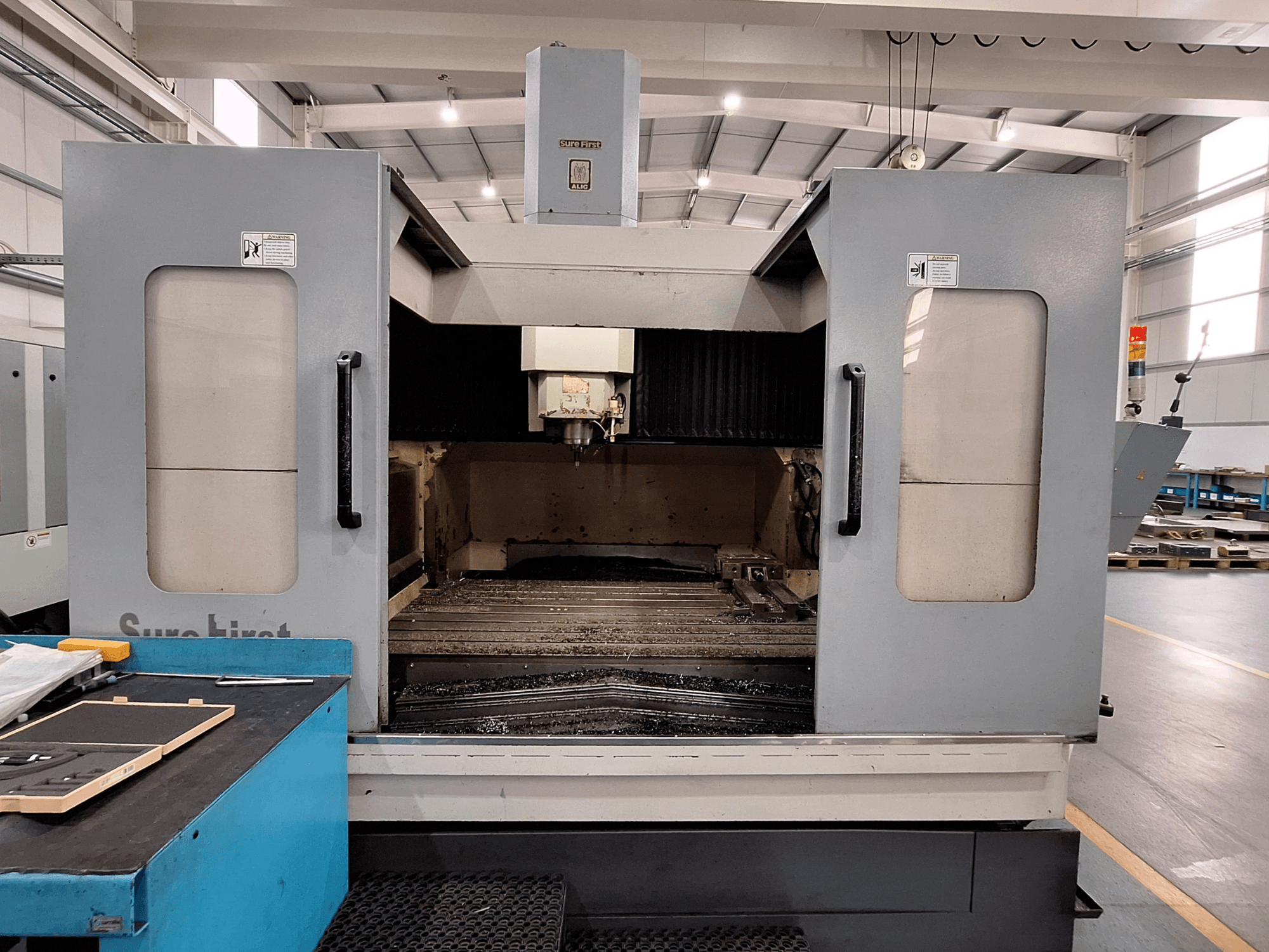 Verticaal bewerkingscentrum Sure First QM-1836, vooraanzicht met gereedschapskop en leeg werkgebied, moderne industriële omgeving.