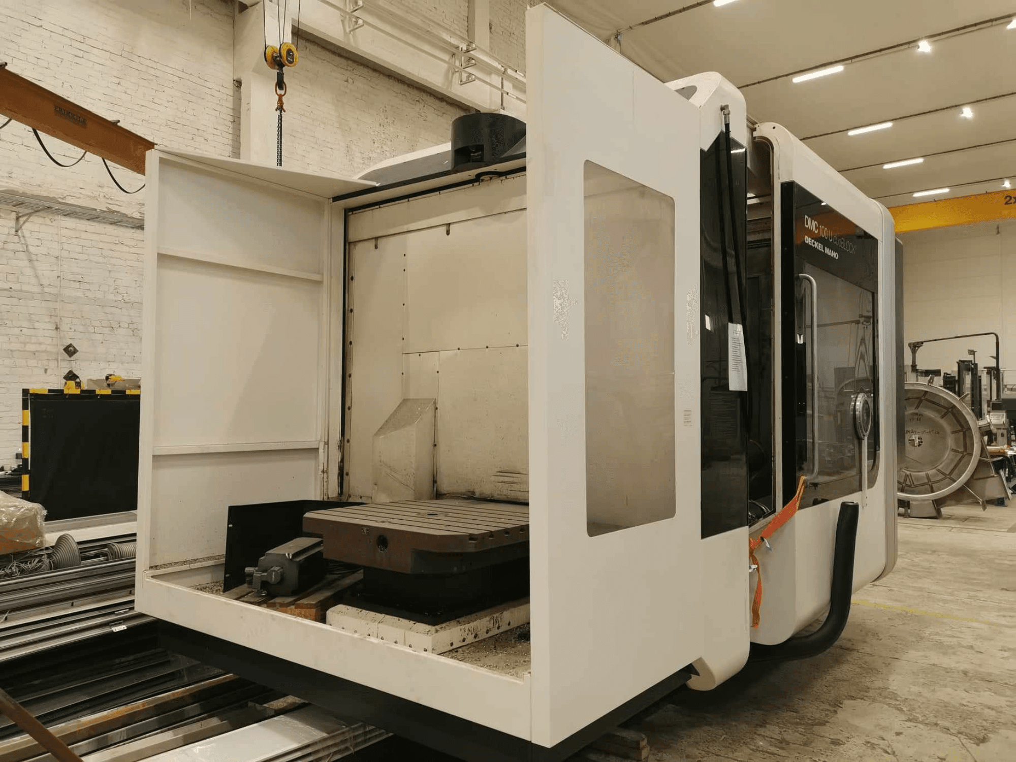 DMC 100U lineaire CNC machine, zijaanzicht met geopende toegangsdeur, waarop de werktafel en interne componenten te zien zijn.