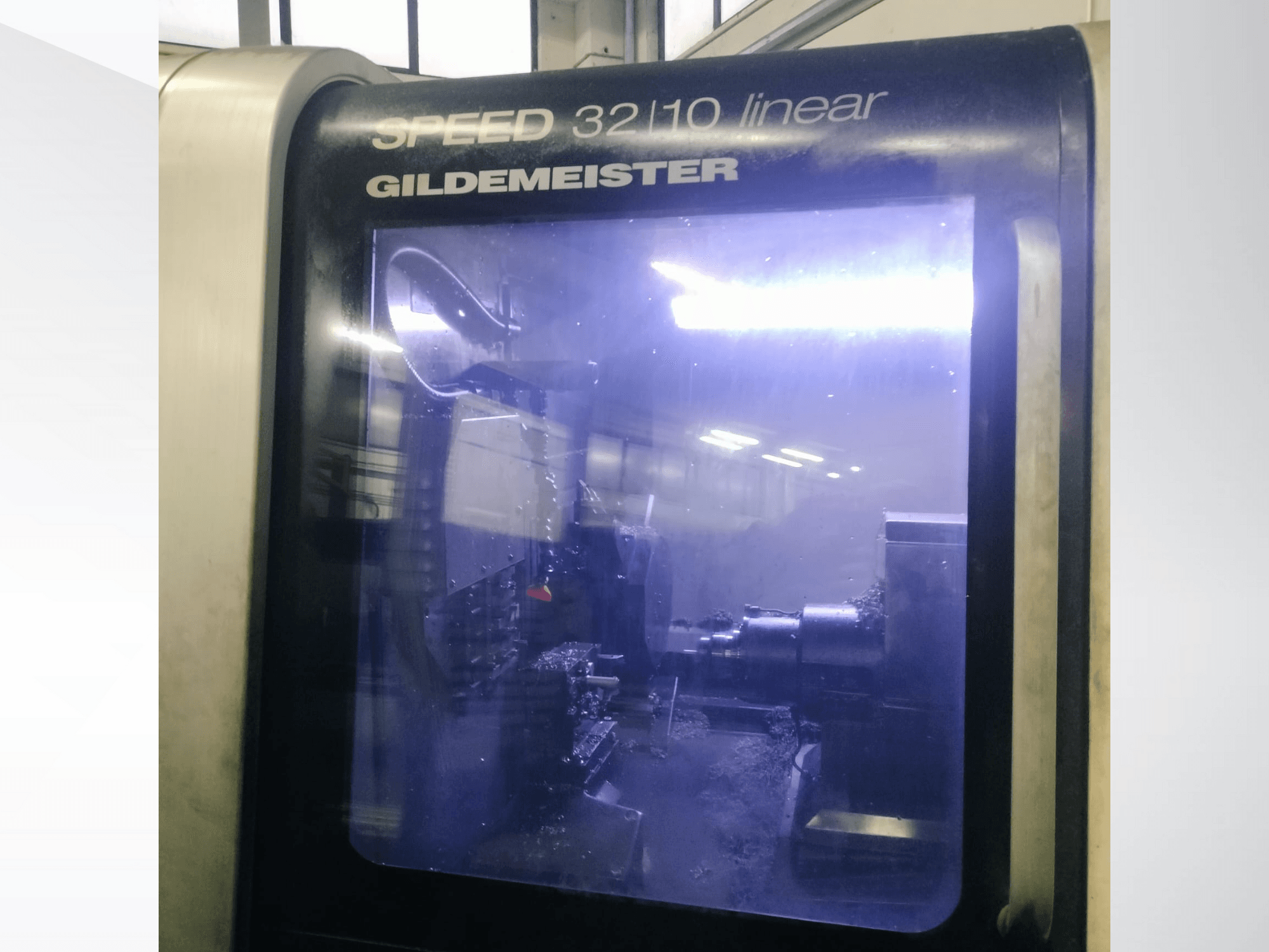 Vooraanzicht van de Gildemeister SPEED 3210 lineaire CNC machine, waarop de interne componenten en het vloeibare koelmiddel in bedrijf te zien zijn.