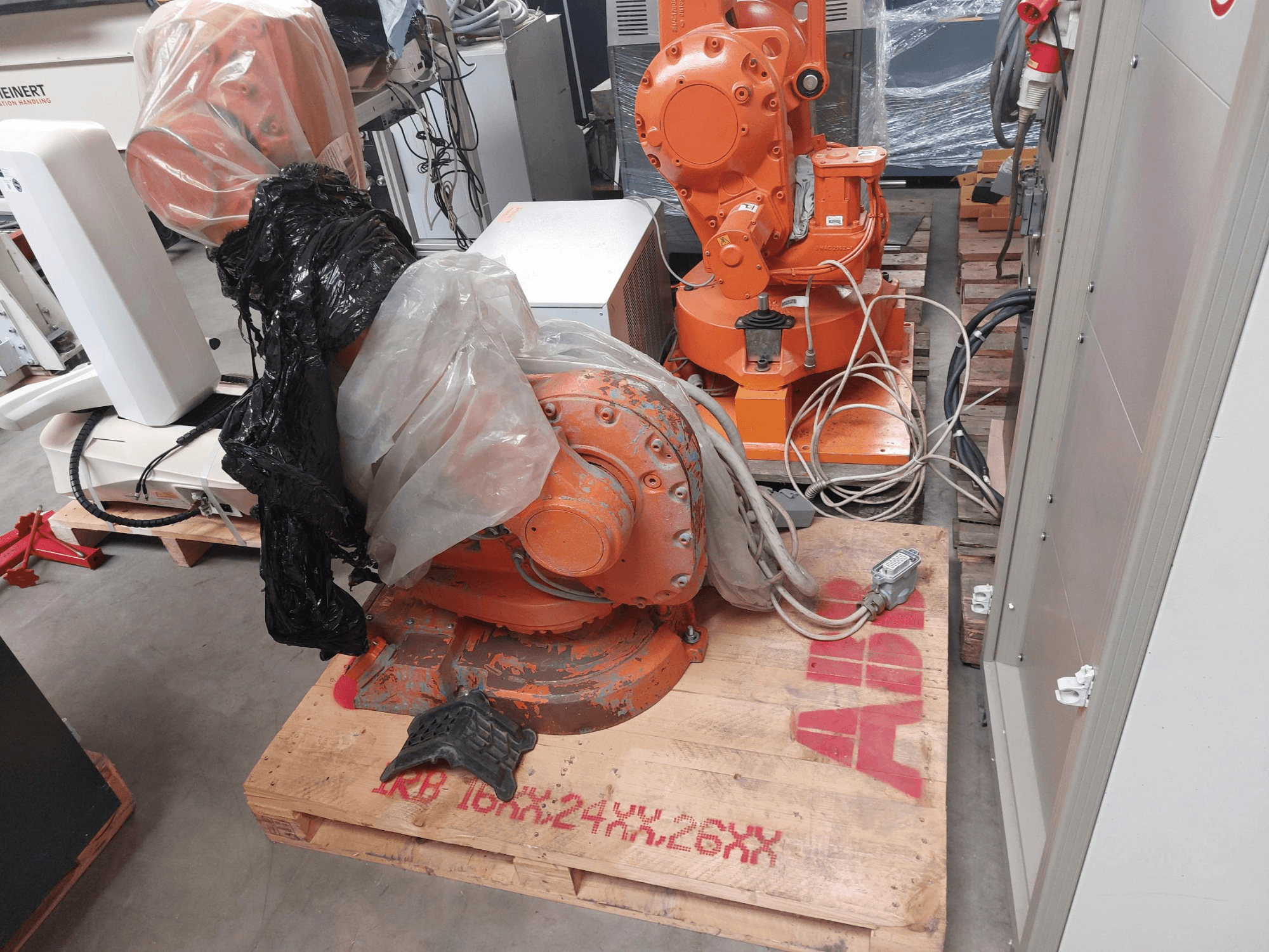 ABB IRB 1600 M2004 robotarm gedeeltelijk bedekt met plastic, gezien vanaf de voorkant, met kabels en extra machines in de buurt.
