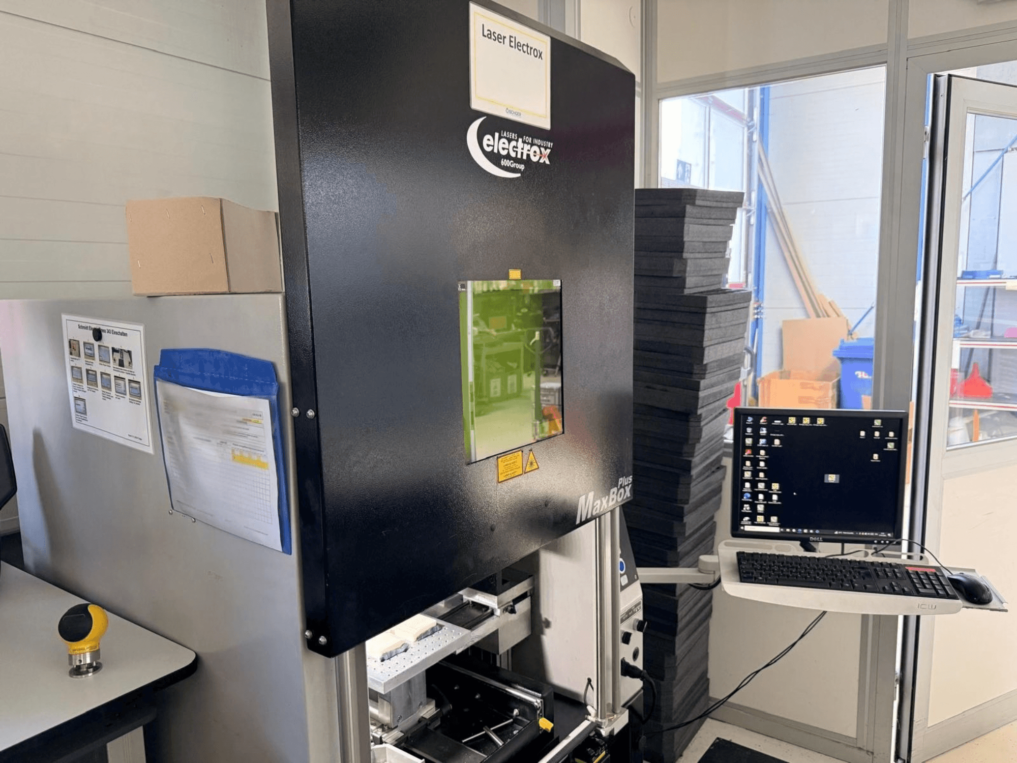 De ELECTROX MaxBox Plus-lasermarkeermachine in zijaanzicht, met een bedieningsscherm, een groen kijkvenster en een werkruimte.