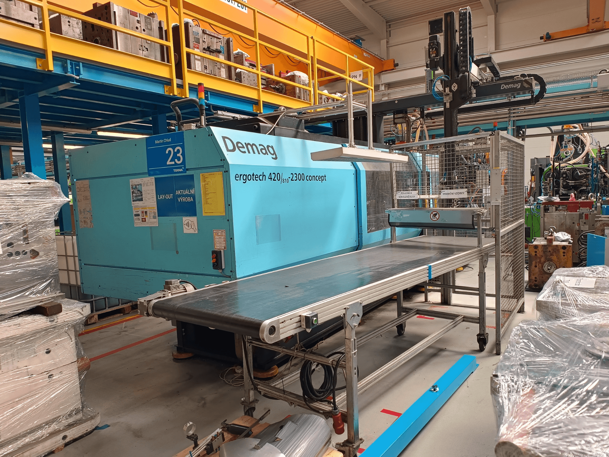 Demag ergotech 420/810 - 2300 hydraulische spuitgietmachine in zijaanzicht, met transportband en veiligheidsomkasting.